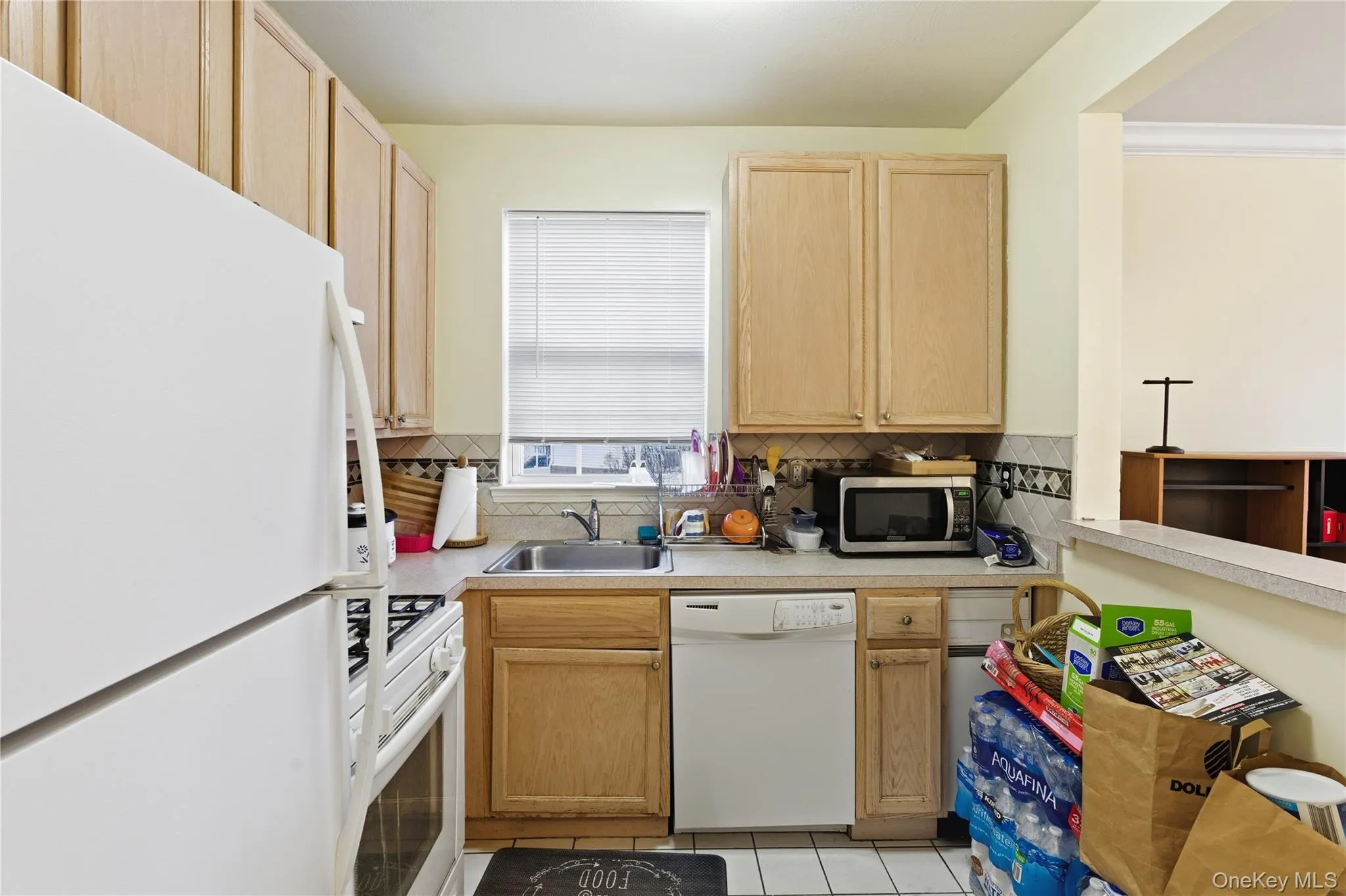 Kitchen featuring light brown cabinetry, white appliances, light countertops, light tile patterned floors, and backsplash Kitchen featuring light brown cabinetry, white appliances, light countertops, light tile patterned floors, and backsplash