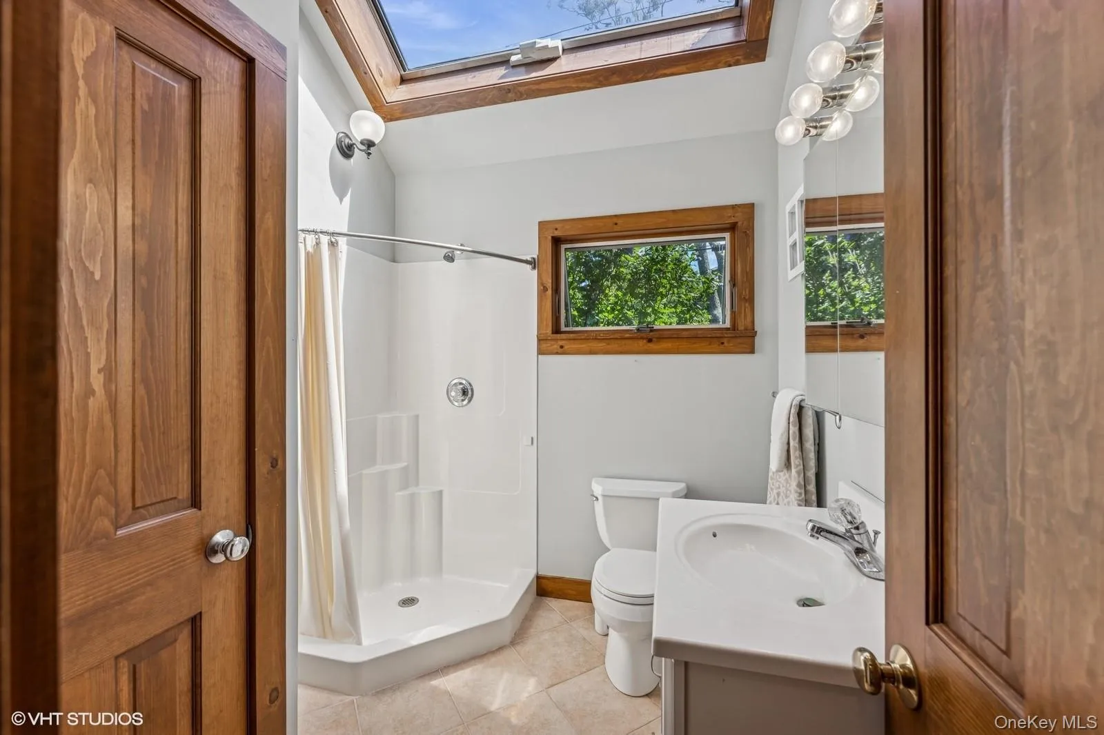 Bathroom with a skylight, vanity, light tile patterned floors, and a shower stall Bathroom with a skylight, vanity, light tile patterned floors, and a shower stall