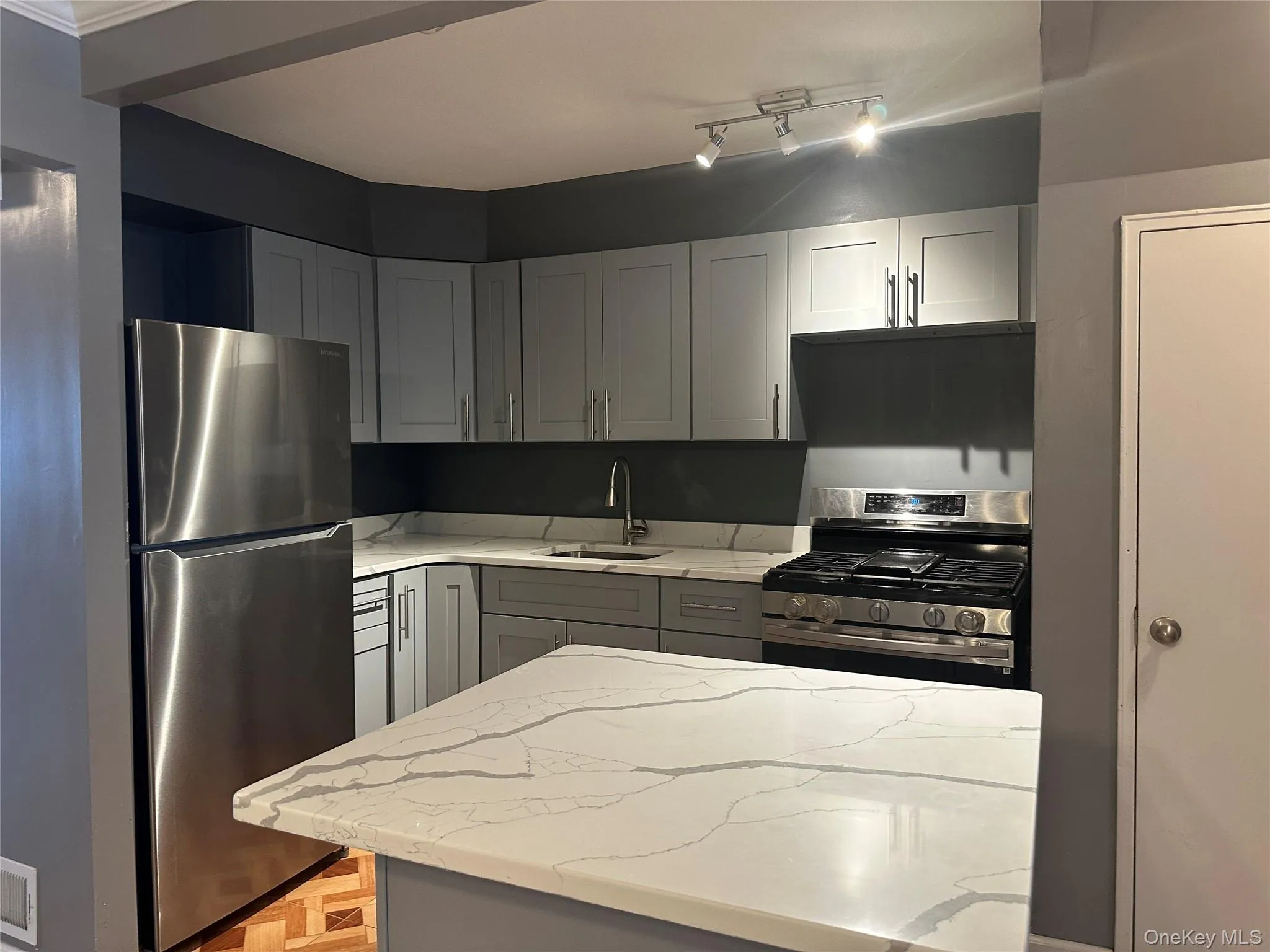 Kitchen featuring gray cabinetry, appliances with stainless steel finishes, light stone counters, and a center island Kitchen featuring gray cabinetry, appliances with stainless steel finishes, light stone counters, and a center island