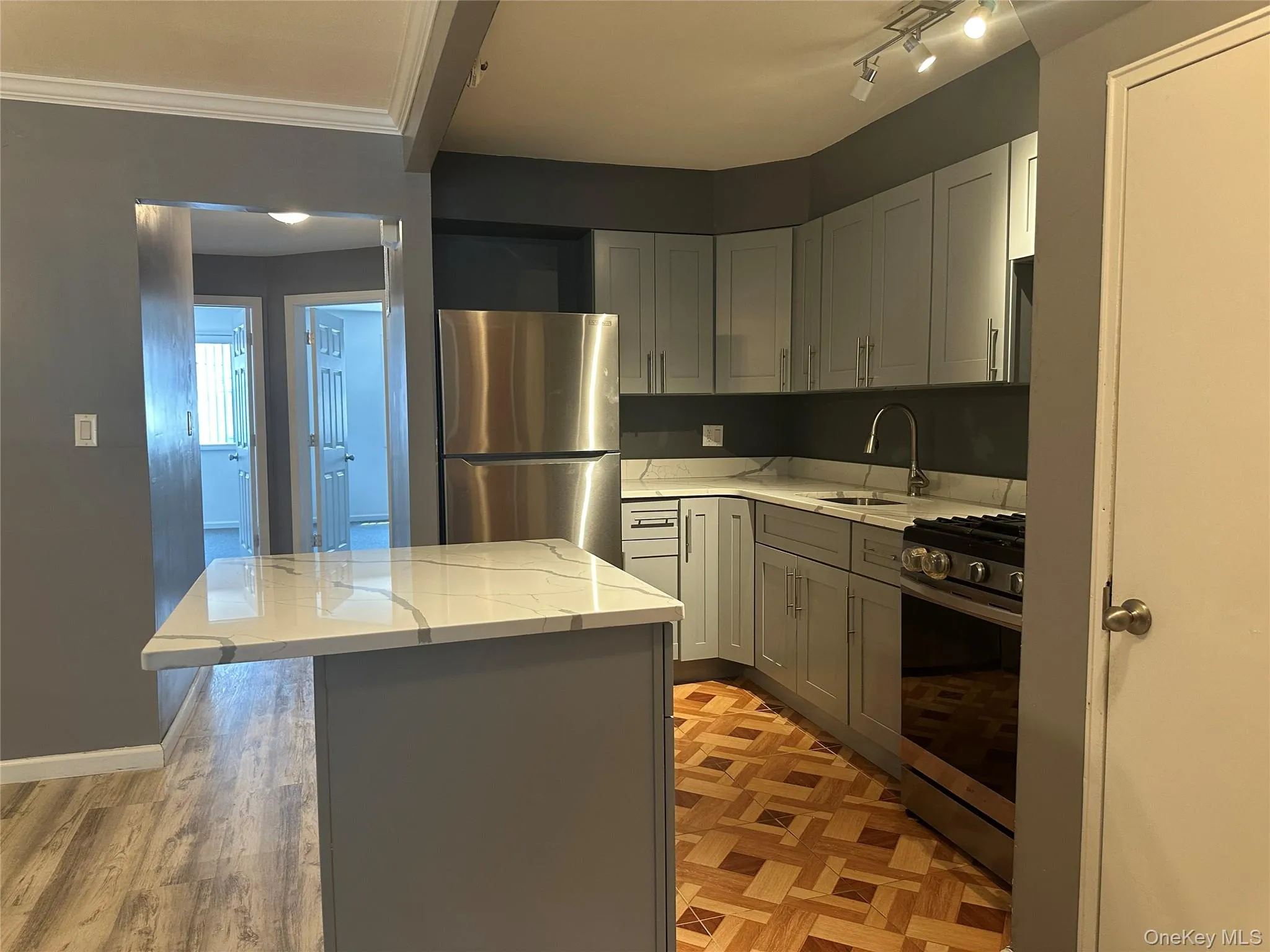 Kitchen with stainless steel appliances, light stone countertops, a kitchen island, gray cabinets, and parquet flooring Kitchen with stainless steel appliances, light stone countertops, a kitchen island, gray cabinets, and parquet flooring