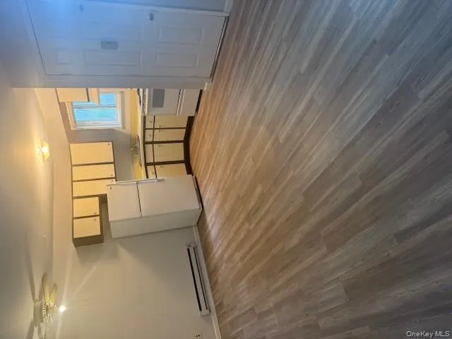 Kitchen with white refrigerator, light wood-type flooring, white cabinets, light countertops, and a baseboard heating unit Kitchen with white refrigerator, light wood-type flooring, white cabinets, light countertops, and a baseboard heating unit
