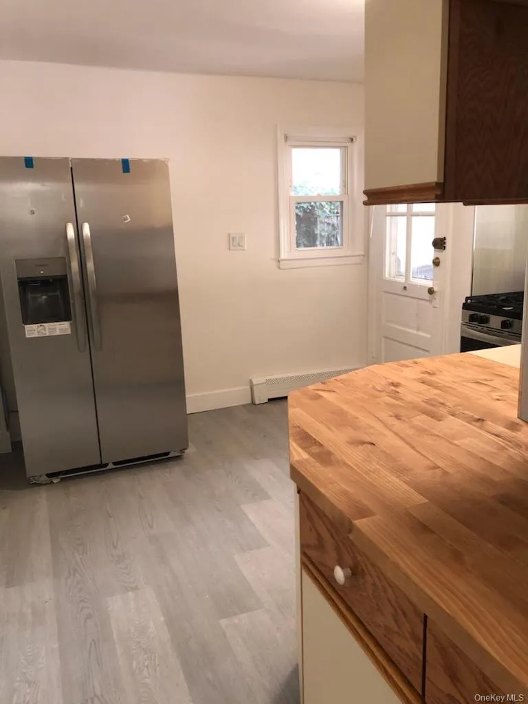 Kitchen featuring butcher block countertops, stainless steel appliances, light wood-type flooring, and baseboard heating Kitchen featuring butcher block countertops, stainless steel appliances, light wood-type flooring, and baseboard heating