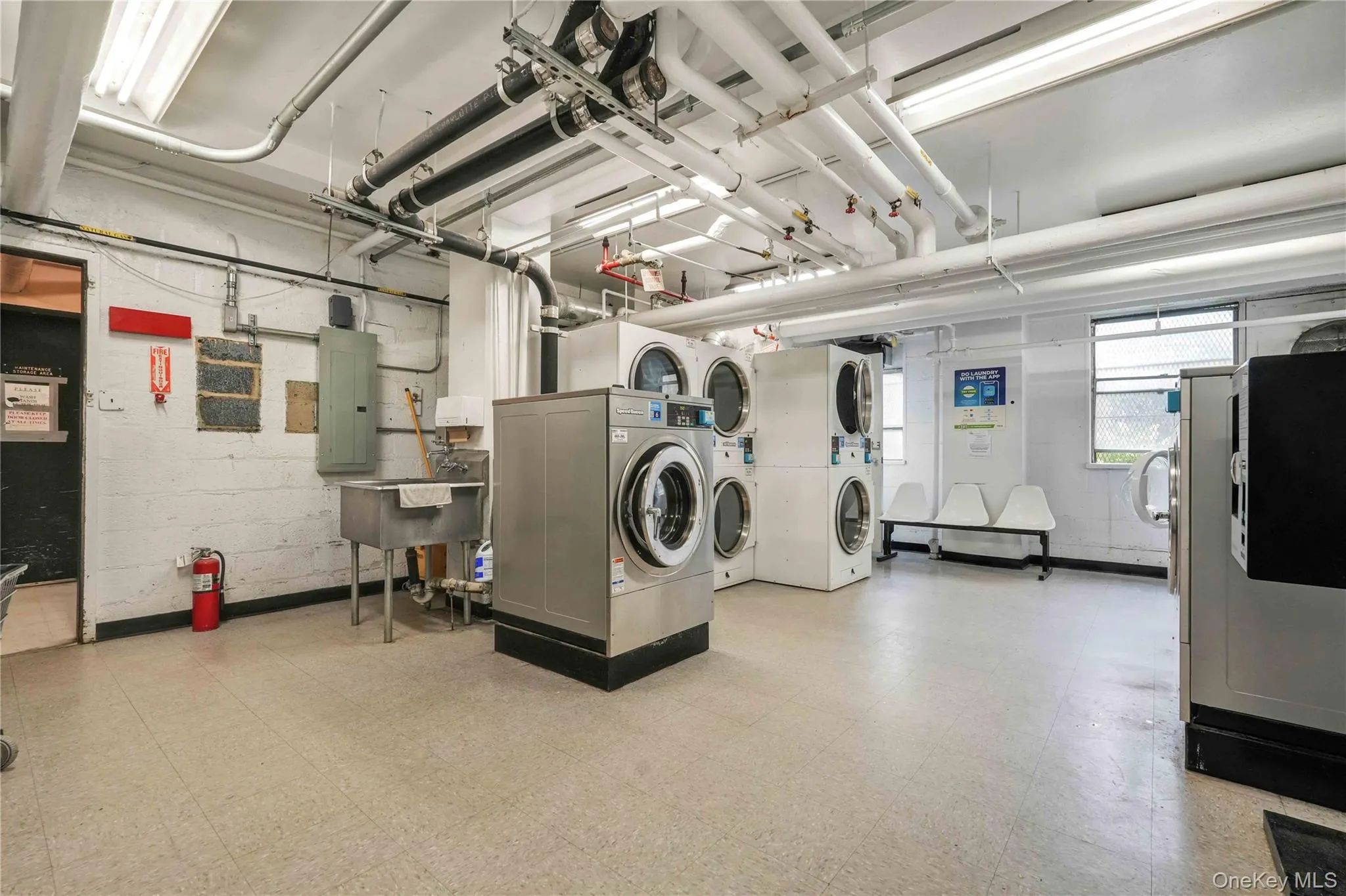 Community laundry with light floors, stacked washer and clothes dryer, concrete block wall, electric panel, and washing machine and clothes dryer Community laundry with light floors, stacked washer and clothes dryer, concrete block wall, electric panel, and washing machine and clothes dryer