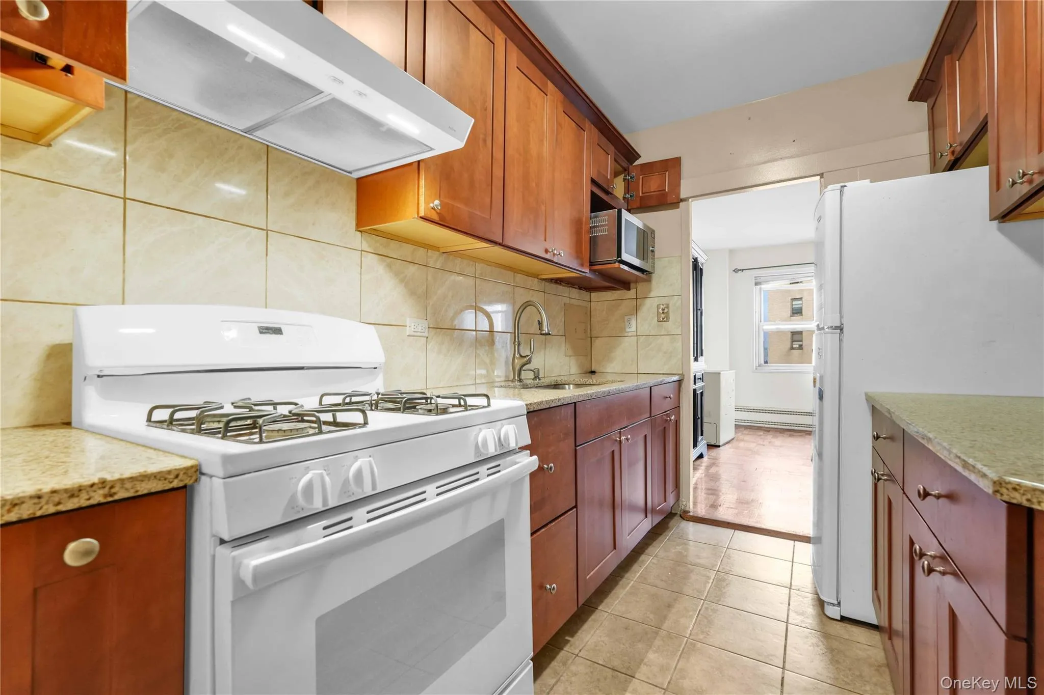 Kitchen with white appliances, exhaust hood, light stone countertops, decorative backsplash, and light tile patterned floors Kitchen with white appliances, exhaust hood, light stone countertops, decorative backsplash, and light tile patterned floors
