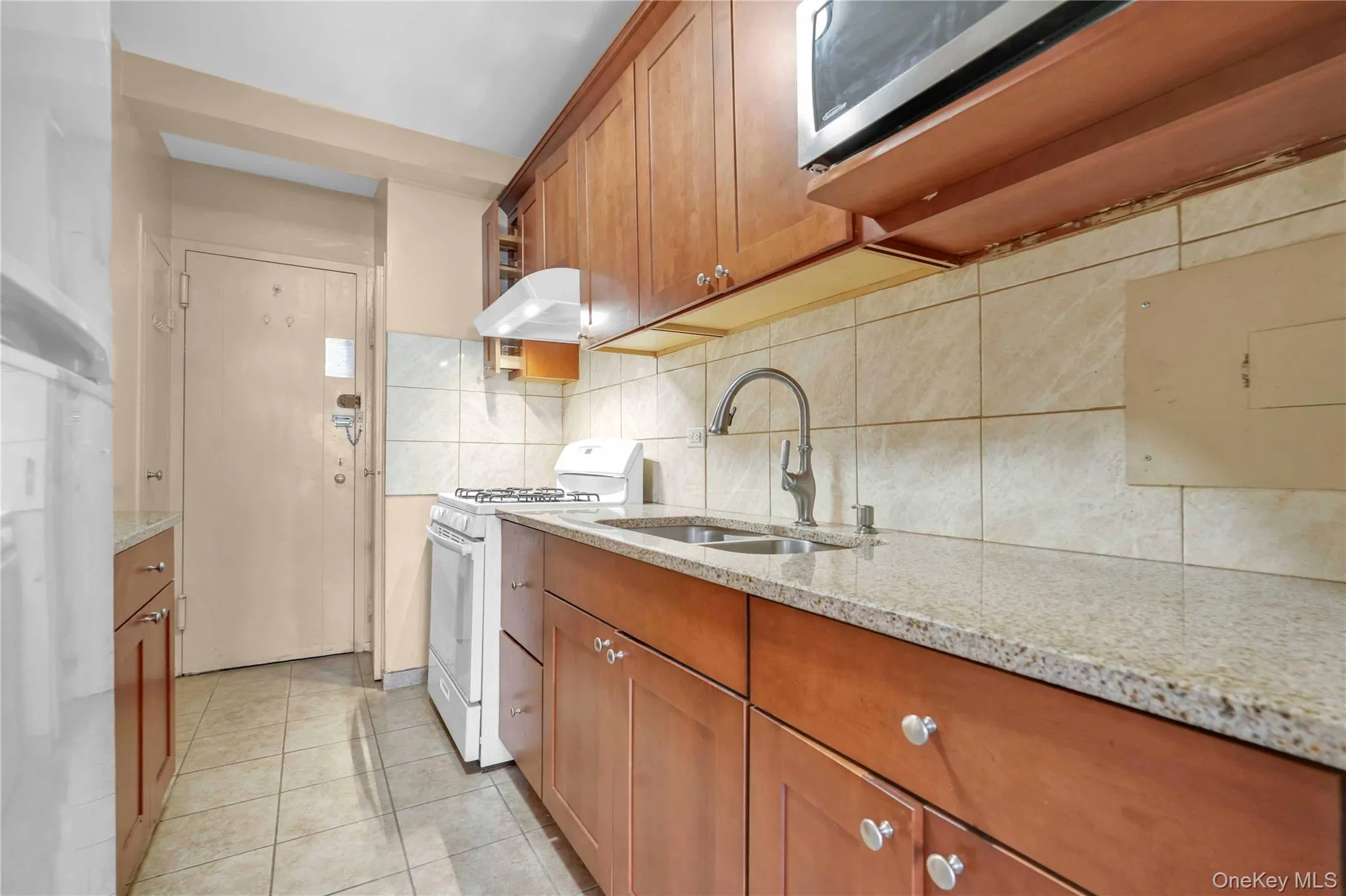 Kitchen with brown cabinets, white gas range, decorative backsplash, light stone countertops, and light tile patterned floors Kitchen with brown cabinets, white gas range, decorative backsplash, light stone countertops, and light tile patterned floors