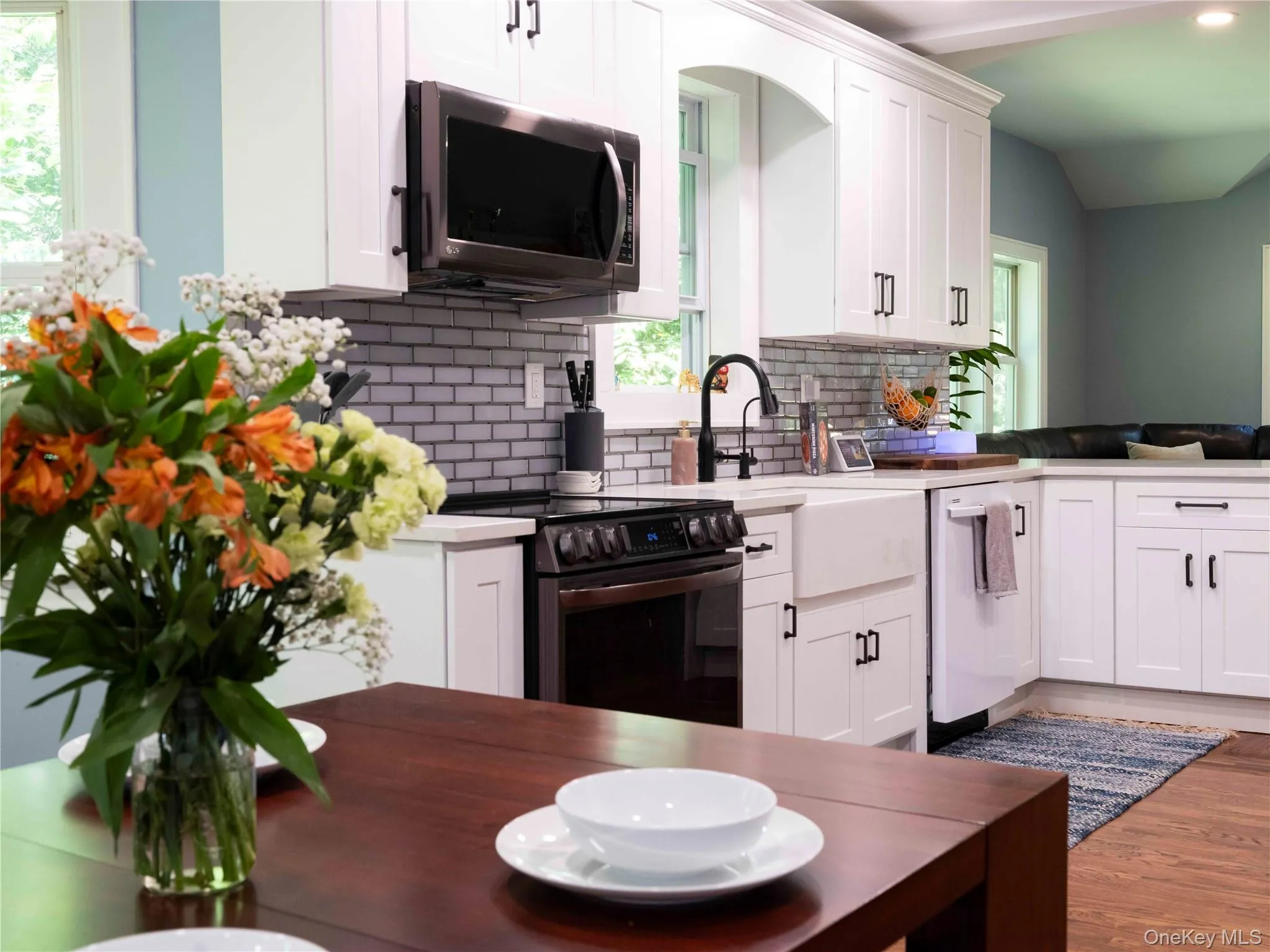 Kitchen featuring white cabinetry, stainless steel appliances, backsplash, and wood finished floors Kitchen featuring white cabinetry, stainless steel appliances, backsplash, and wood finished floors