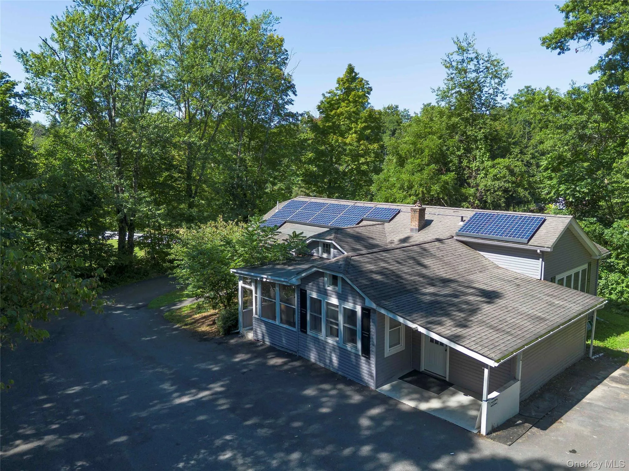 View of front of property featuring solar panels, a sunroom, driveway, a chimney, and roof with shingles View of front of property featuring solar panels, a sunroom, driveway, a chimney, and roof with shingles