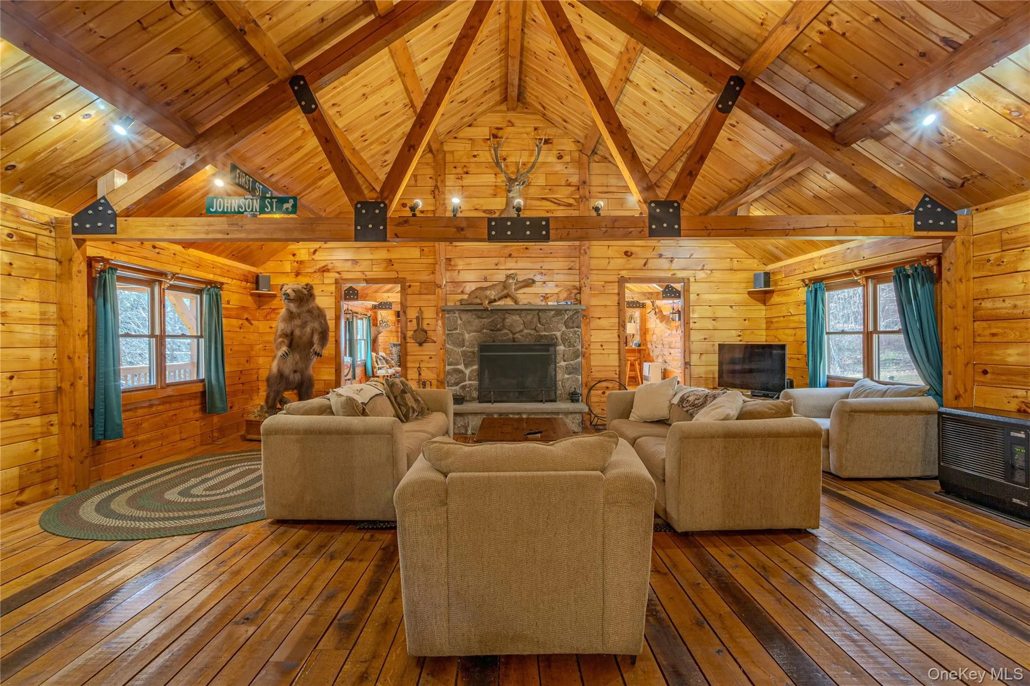 Living room featuring hardwood / wood-style floors, a stone fireplace, a wooden ceiling with exposed beams, wood walls, and high vaulted ceiling Living room featuring hardwood / wood-style floors, a stone fireplace, a wooden ceiling with exposed beams, wood walls, and high vaulted ceiling