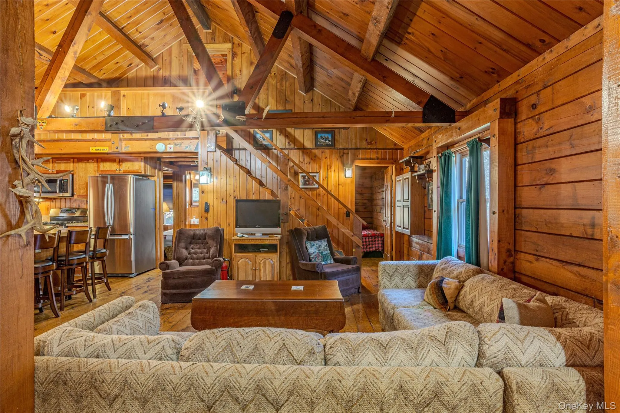 Living area featuring wood walls, a wood ceiling with exposed beams, high vaulted ceiling, stairway, and light wood-style flooring Living area featuring wood walls, a wood ceiling with exposed beams, high vaulted ceiling, stairway, and light wood-style flooring