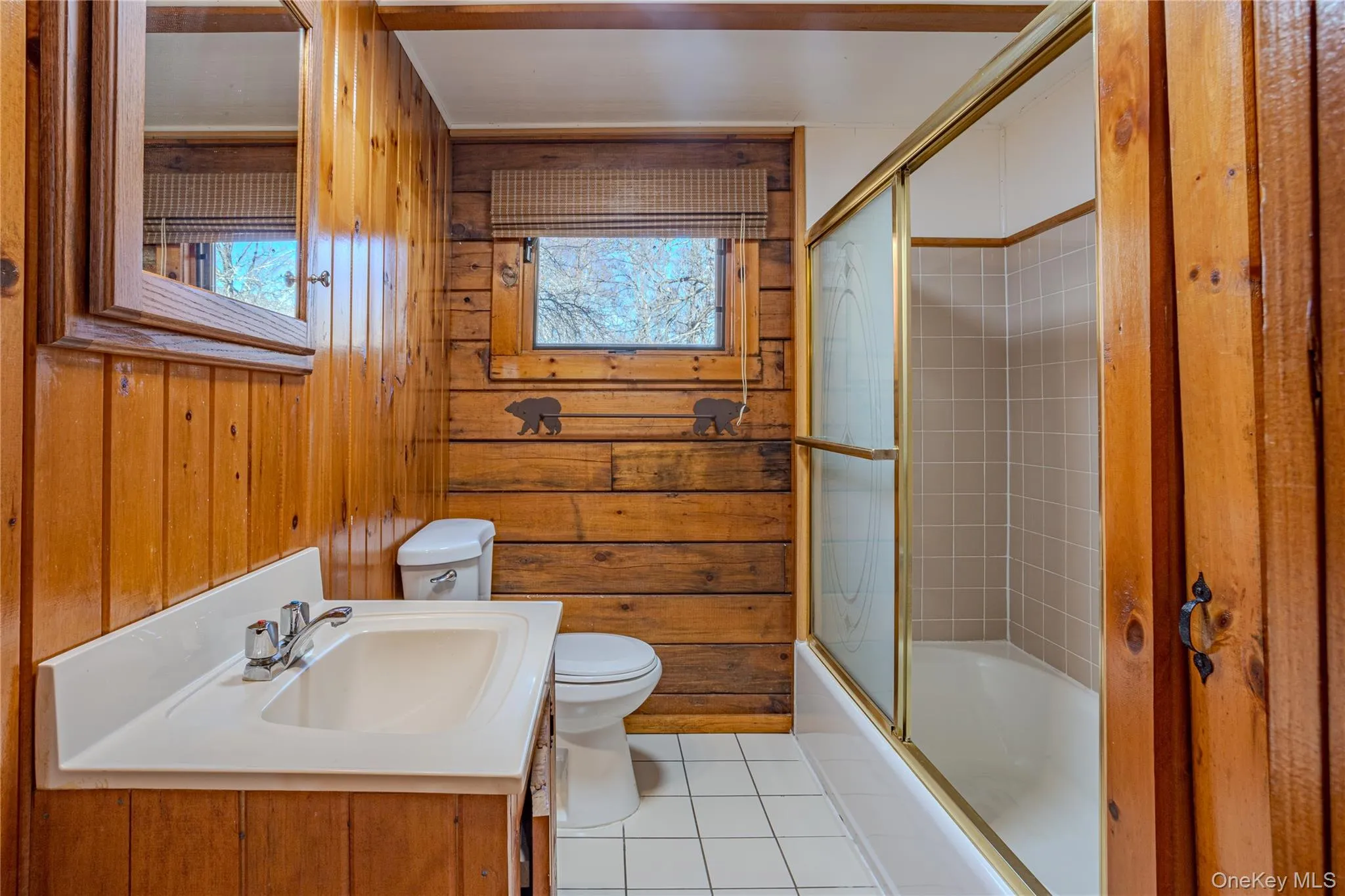 Full bathroom featuring enclosed tub / shower combo, healthy amount of natural light, light tile patterned floors, vanity, and wooden walls Full bathroom featuring enclosed tub / shower combo, healthy amount of natural light, light tile patterned floors, vanity, and wooden walls