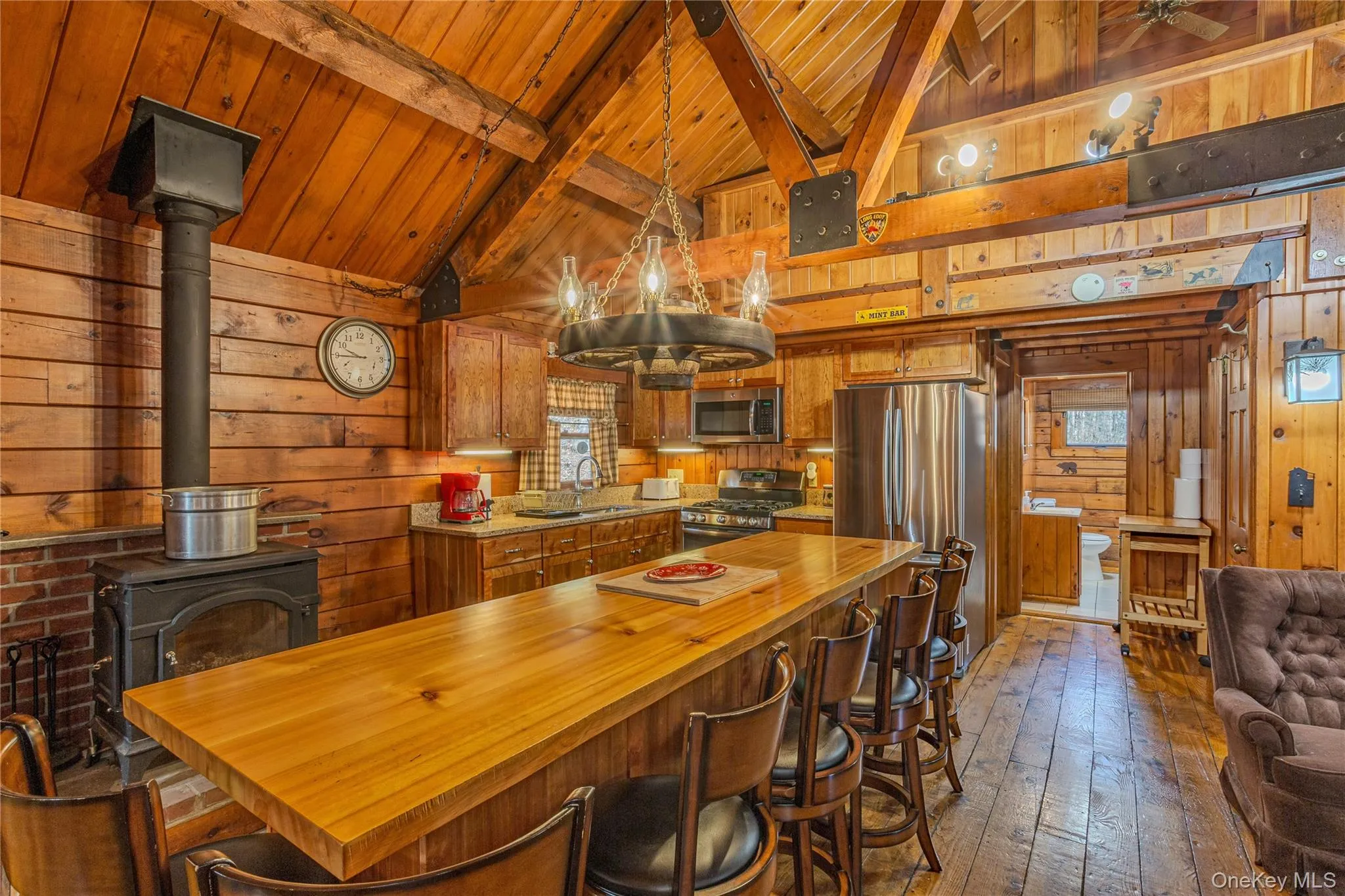 Kitchen featuring wood walls, a wood stove, appliances with stainless steel finishes, hardwood / wood-style flooring, and brown cabinetry Kitchen featuring wood walls, a wood stove, appliances with stainless steel finishes, hardwood / wood-style flooring, and brown cabinetry