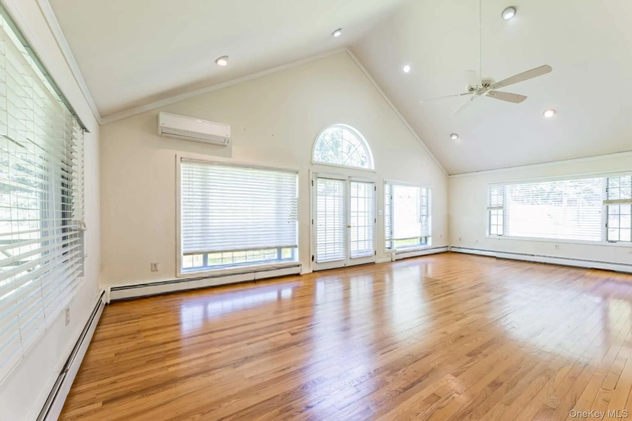 Unfurnished living room with plenty of natural light, a baseboard heating unit, light wood-style floors, crown molding, and high vaulted ceiling Unfurnished living room with plenty of natural light, a baseboard heating unit, light wood-style floors, crown molding, and high vaulted ceiling