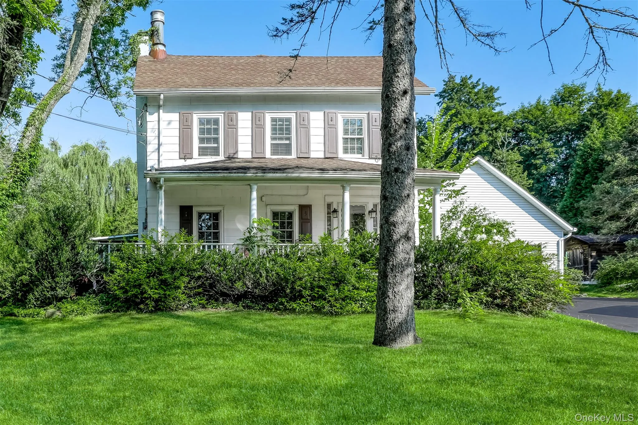 Colonial home with a front lawn, a chimney, covered porch, and roof with shingles Colonial home with a front lawn, a chimney, covered porch, and roof with shingles