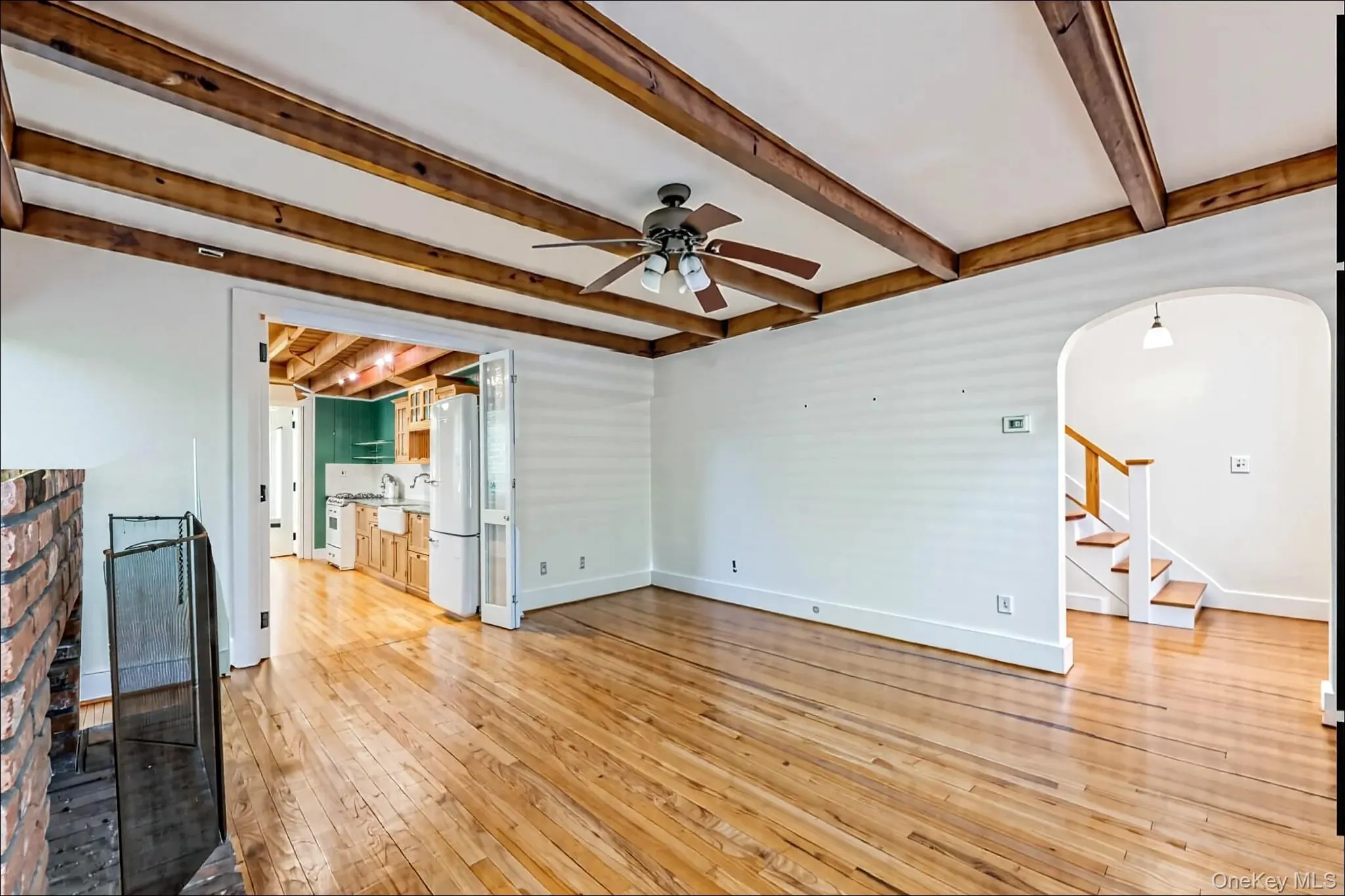 Unfurnished living room with a ceiling fan, arched walkways, stairway, light wood-style floors, and beamed ceiling Unfurnished living room with a ceiling fan, arched walkways, stairway, light wood-style floors, and beamed ceiling