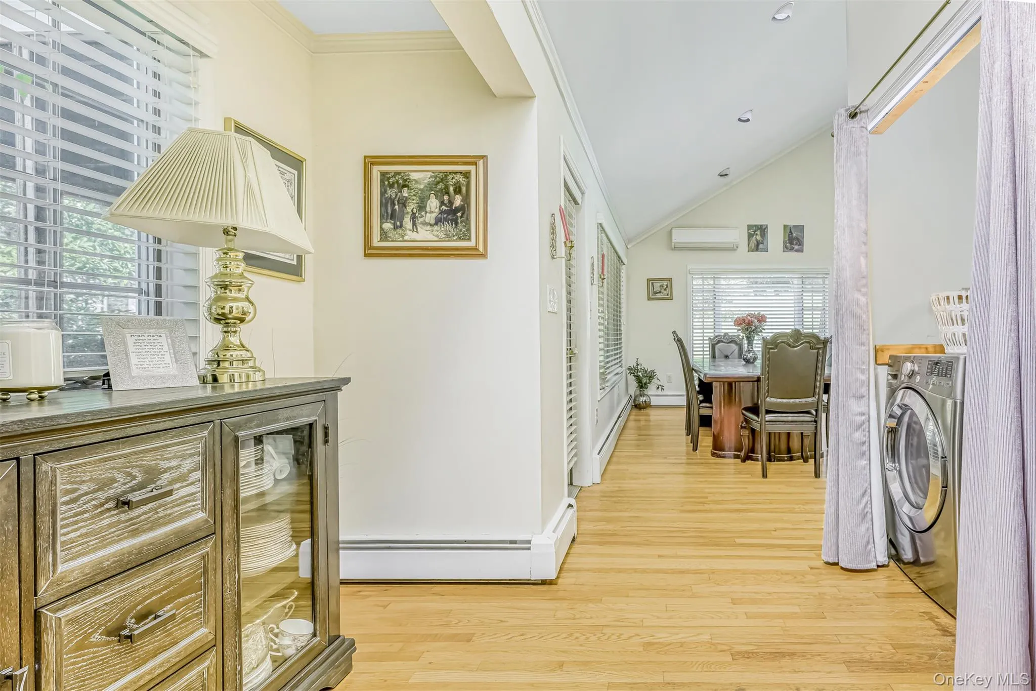 Hallway featuring light wood finished floors, ornamental molding, a wall mounted air conditioner, and lofted ceiling Hallway featuring light wood finished floors, ornamental molding, a wall mounted air conditioner, and lofted ceiling