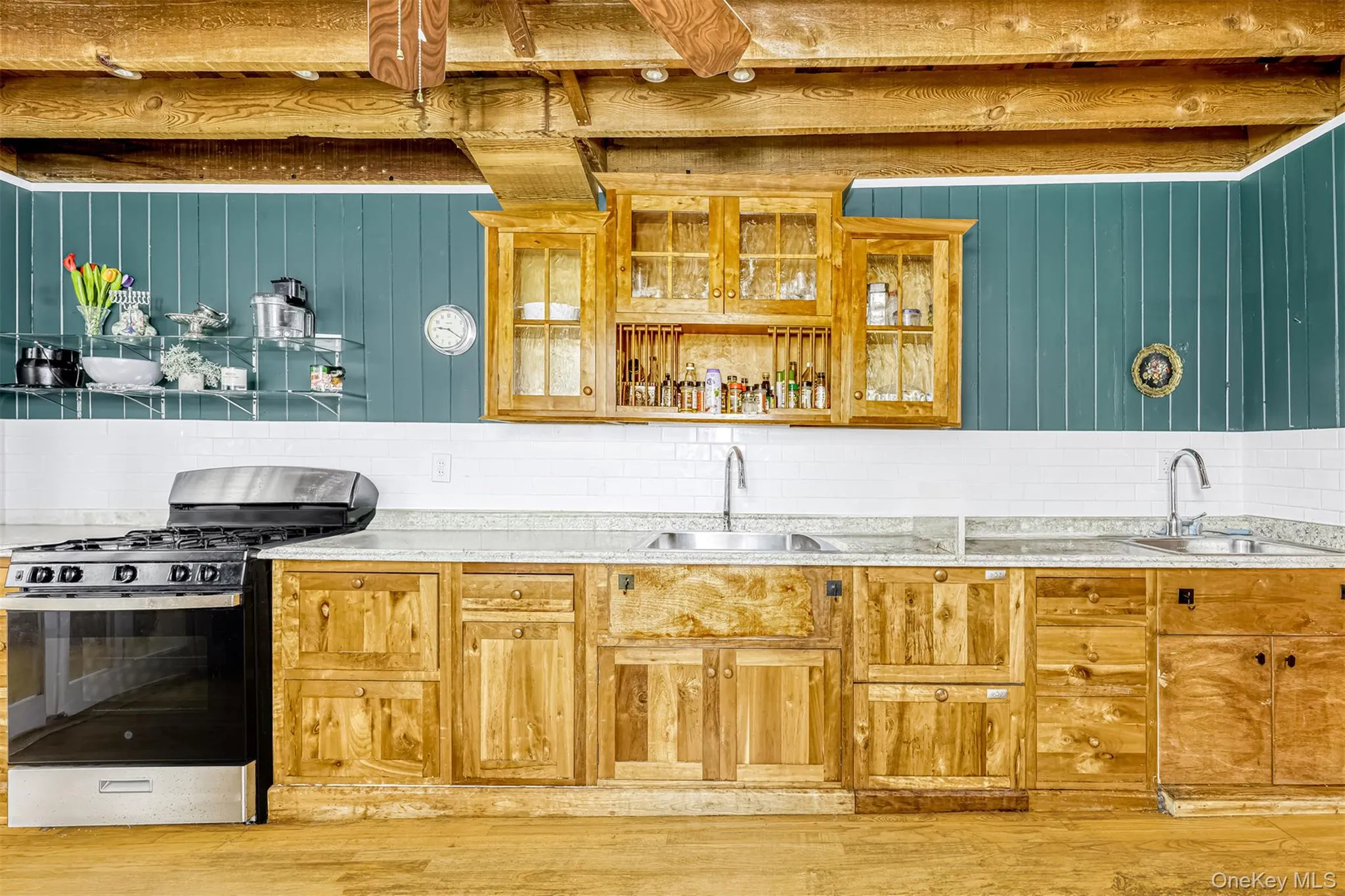 Kitchen featuring stainless steel gas stove, backsplash, light wood-style flooring, glass insert cabinets, and beamed ceiling Kitchen featuring stainless steel gas stove, backsplash, light wood-style flooring, glass insert cabinets, and beamed ceiling