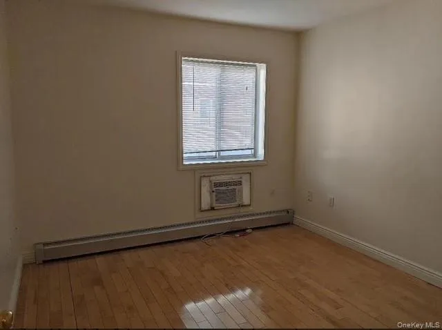Spare room featuring baseboard heating, light wood-style flooring, and an AC wall unit Spare room featuring baseboard heating, light wood-style flooring, and an AC wall unit