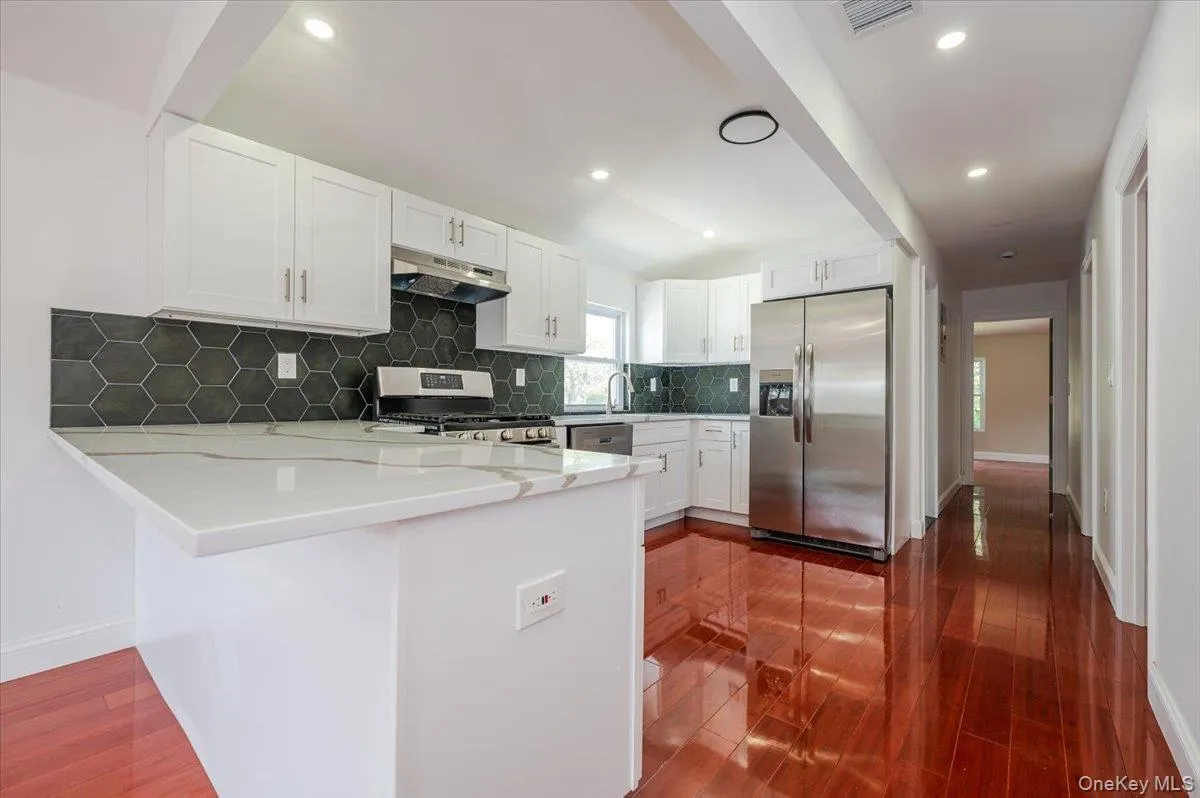 Kitchen with appliances with stainless steel finishes, white cabinetry, light stone countertops, backsplash, and a peninsula Kitchen with appliances with stainless steel finishes, white cabinetry, light stone countertops, backsplash, and a peninsula