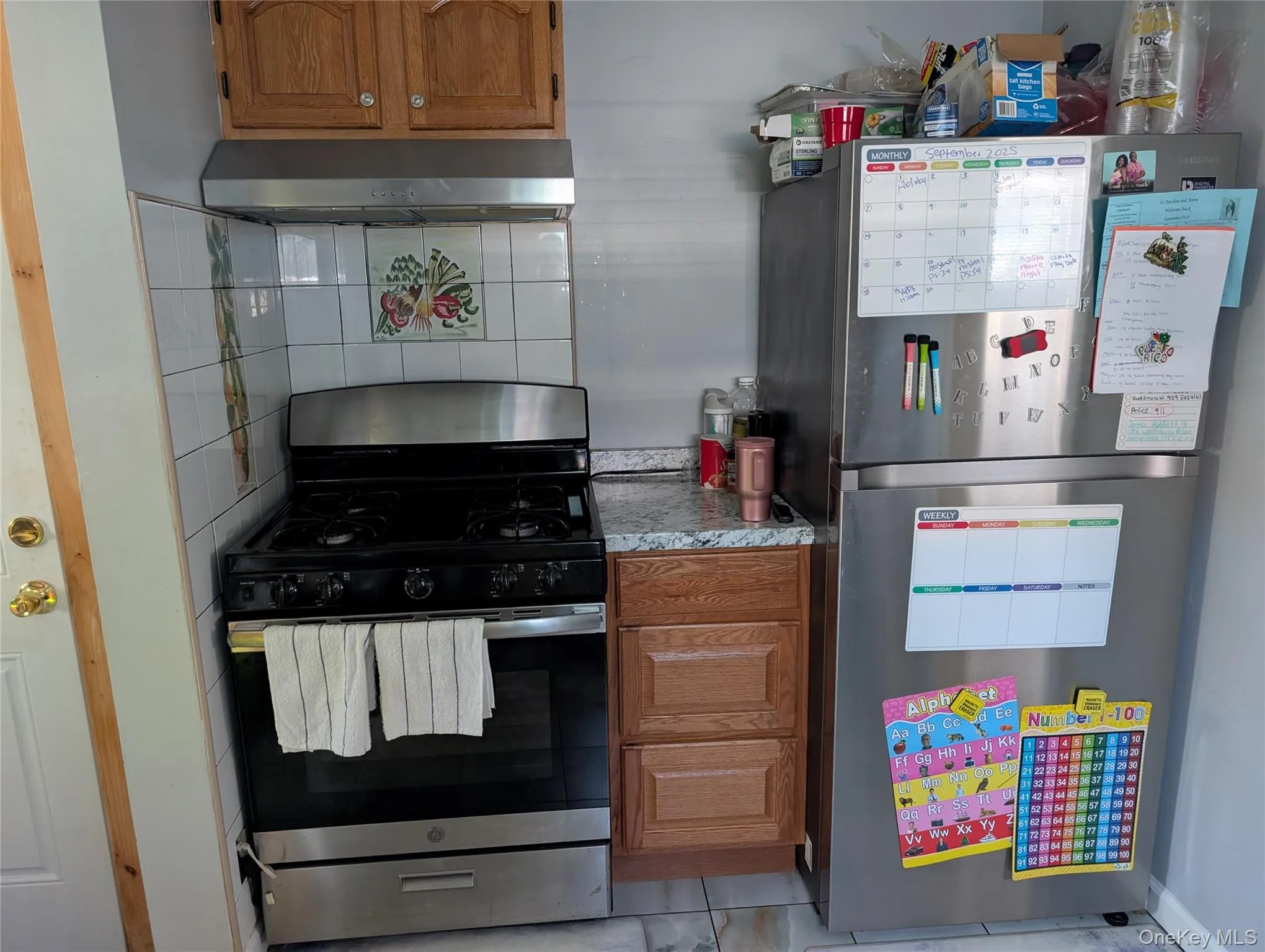 Kitchen with brown cabinets, appliances with stainless steel finishes, light countertops, and exhaust hood Kitchen with brown cabinets, appliances with stainless steel finishes, light countertops, and exhaust hood
