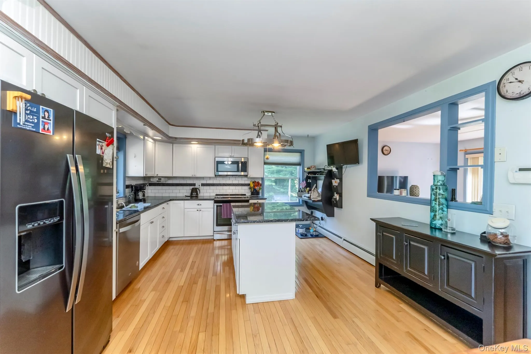 Kitchen with appliances with stainless steel finishes, light wood-style flooring, tasteful backsplash, dark stone counters, and a kitchen island Kitchen with appliances with stainless steel finishes, light wood-style flooring, tasteful backsplash, dark stone counters, and a kitchen island