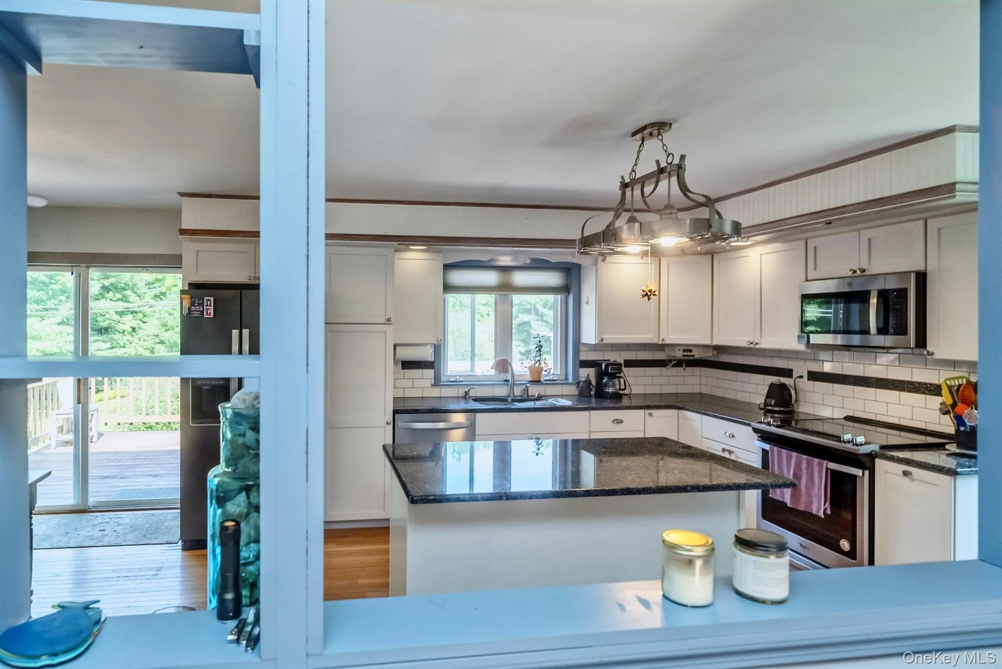 Kitchen with stainless steel appliances, backsplash, hanging light fixtures, dark stone counters, and wood finished floors Kitchen with stainless steel appliances, backsplash, hanging light fixtures, dark stone counters, and wood finished floors