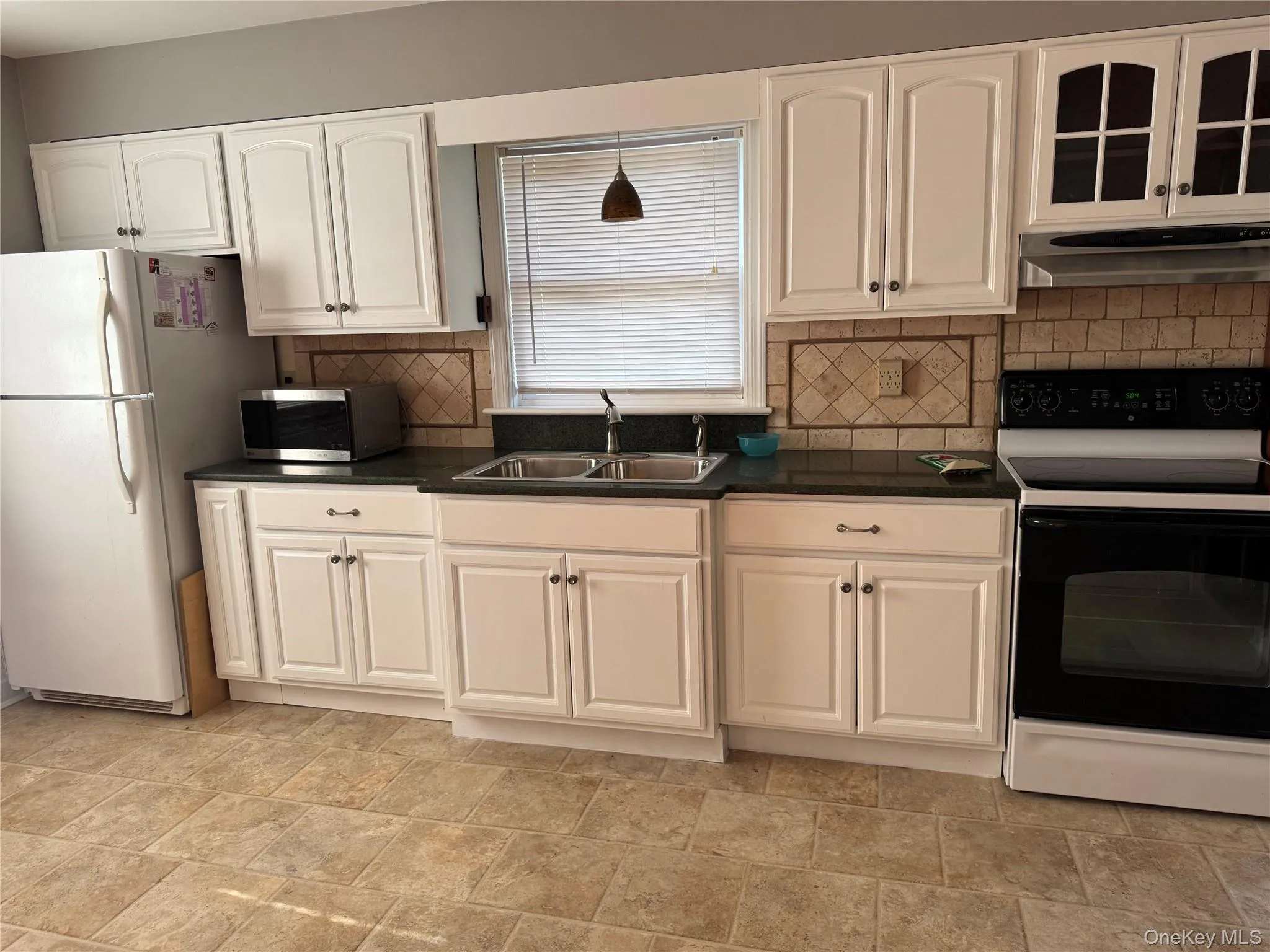 Kitchen with electric range oven, freestanding refrigerator, white cabinetry, under cabinet range hood, and stainless steel microwave Kitchen with electric range oven, freestanding refrigerator, white cabinetry, under cabinet range hood, and stainless steel microwave