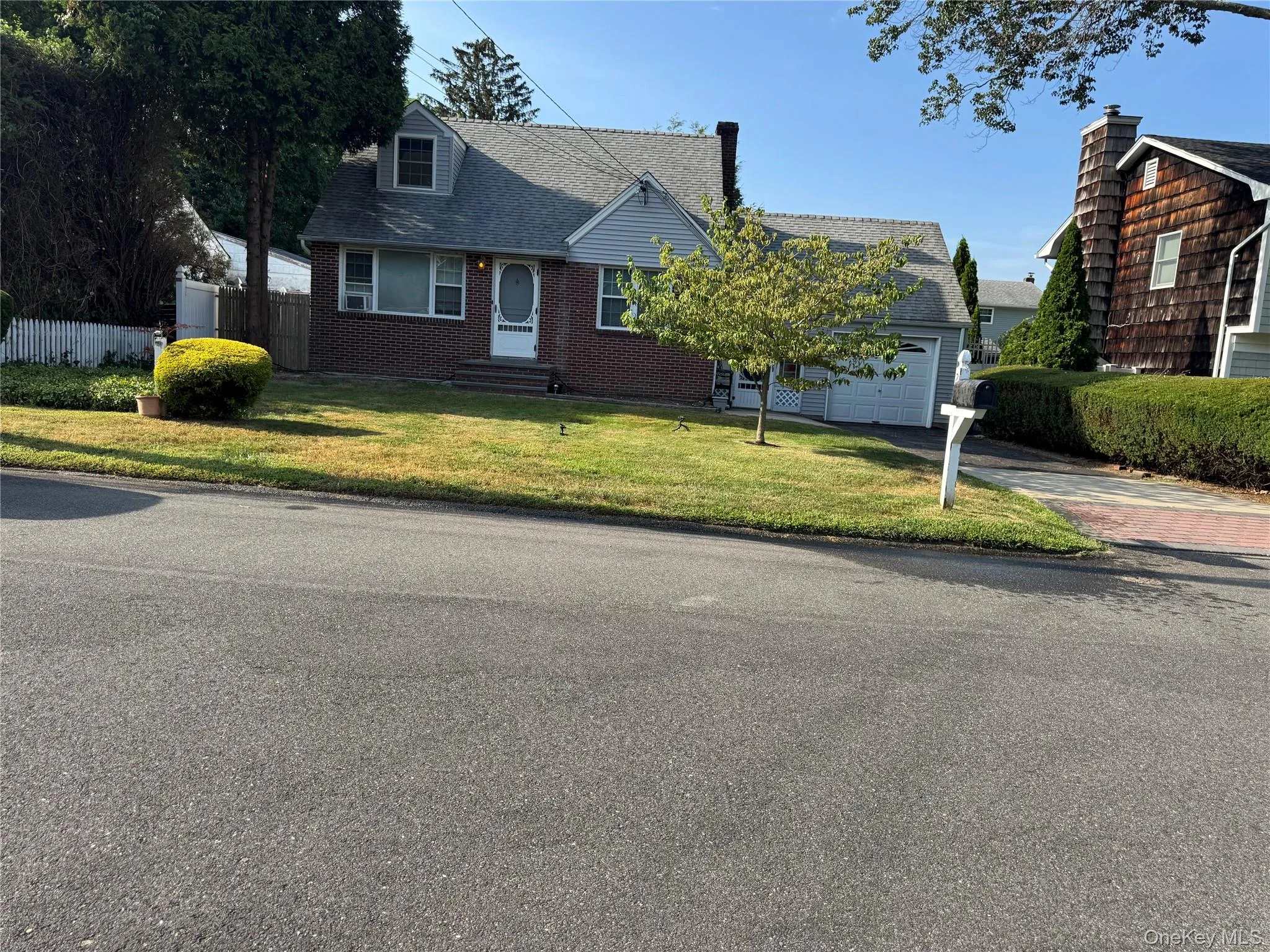 Cape cod home featuring driveway, brick siding, a shingled roof, and an attached garage Cape cod home featuring driveway, brick siding, a shingled roof, and an attached garage