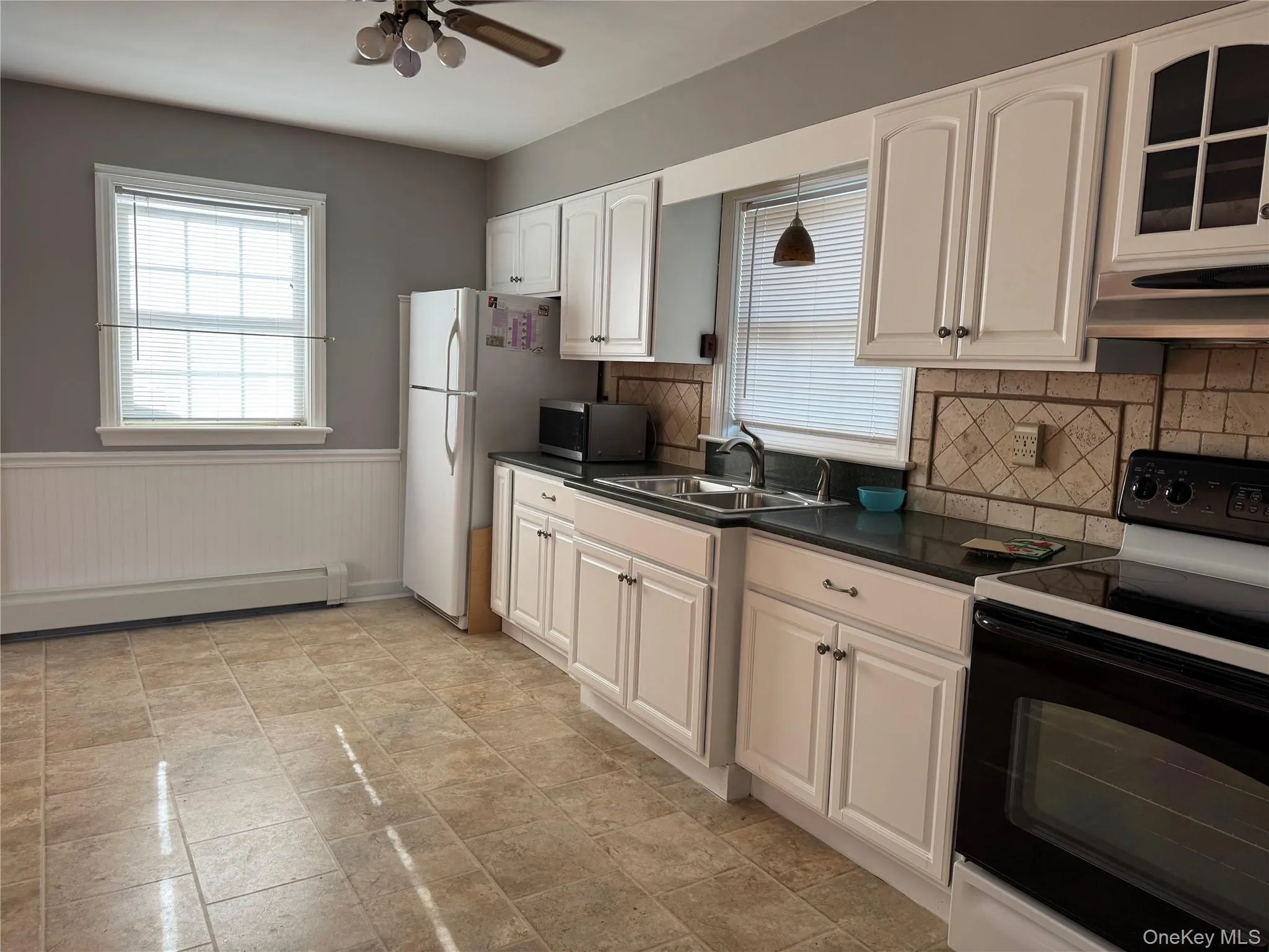 Kitchen with electric range oven, a wainscoted wall, dark countertops, tasteful backsplash, and white cabinetry Kitchen with electric range oven, a wainscoted wall, dark countertops, tasteful backsplash, and white cabinetry