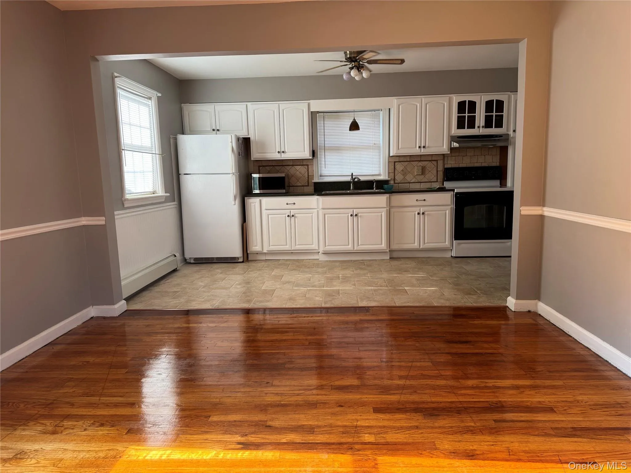Kitchen with tasteful backsplash, light wood-style floors, dark countertops, freestanding refrigerator, and electric stove Kitchen with tasteful backsplash, light wood-style floors, dark countertops, freestanding refrigerator, and electric stove
