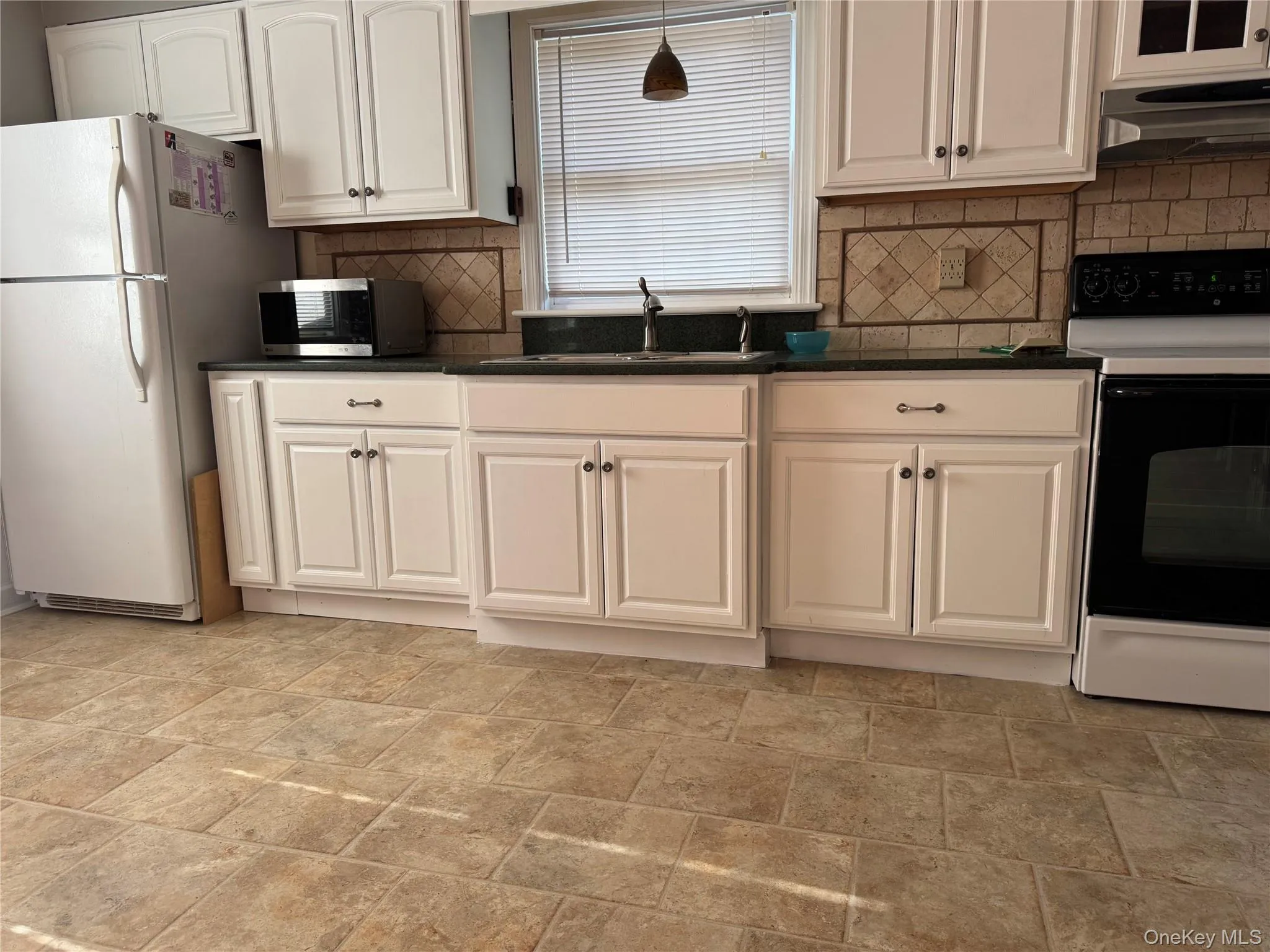 Kitchen featuring range with electric stovetop, freestanding refrigerator, under cabinet range hood, stainless steel microwave, and white cabinets Kitchen featuring range with electric stovetop, freestanding refrigerator, under cabinet range hood, stainless steel microwave, and white cabinets