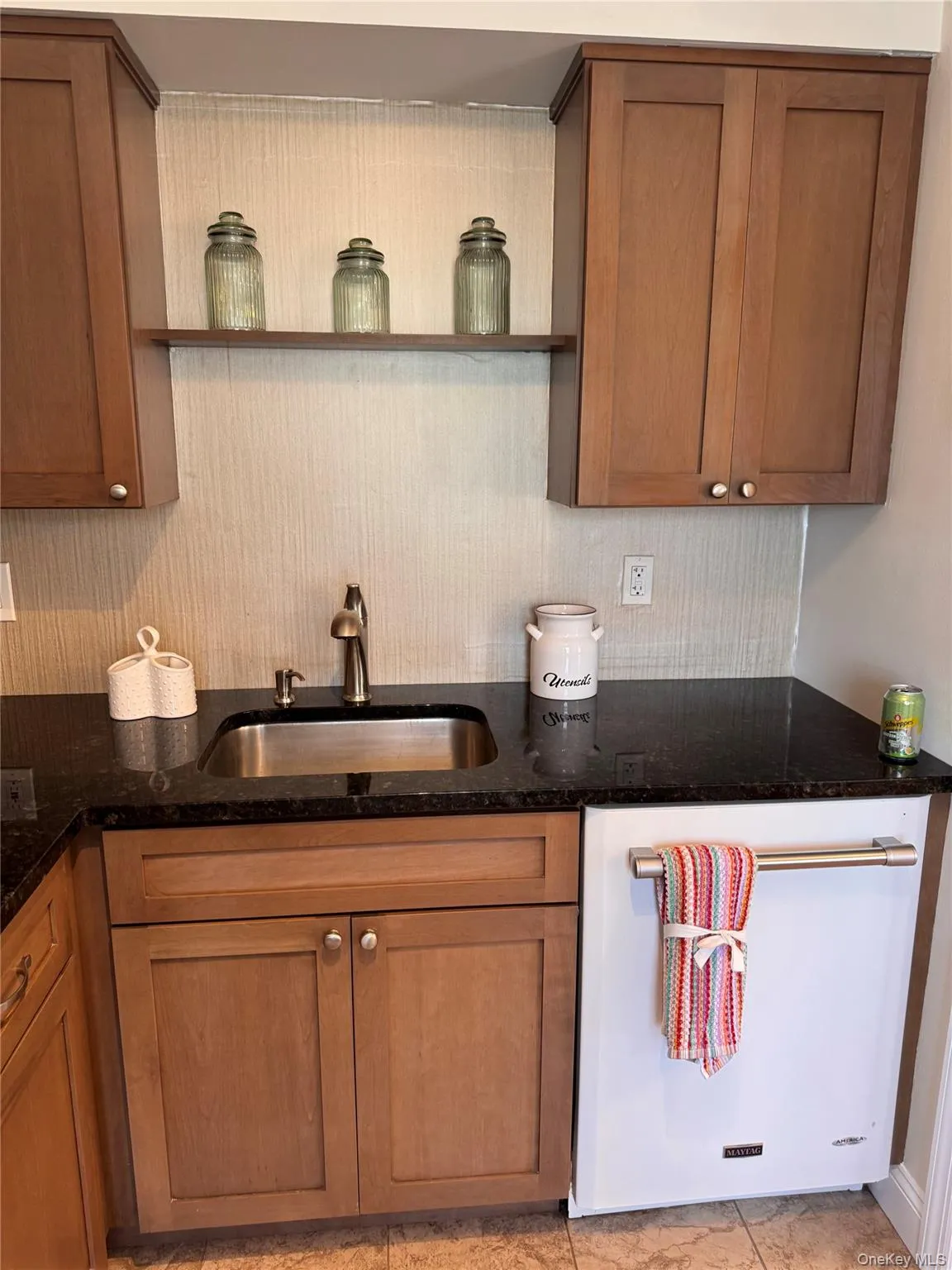 Kitchen featuring white dishwasher, dark stone countertops, brown cabinetry, and open shelves Kitchen featuring white dishwasher, dark stone countertops, brown cabinetry, and open shelves