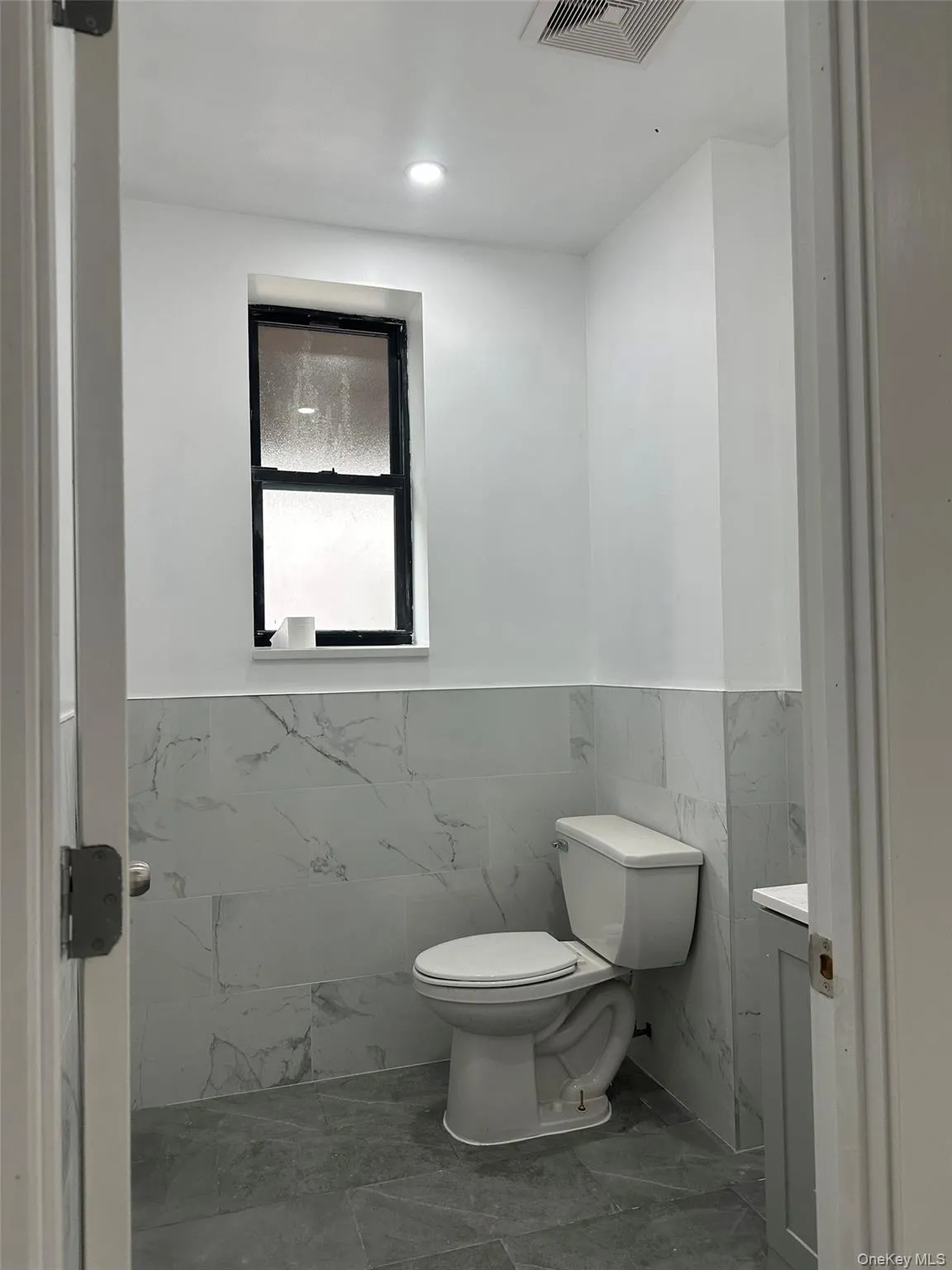 Bathroom featuring vanity, tile walls, a wainscoted wall, and marble look tiles Bathroom featuring vanity, tile walls, a wainscoted wall, and marble look tiles