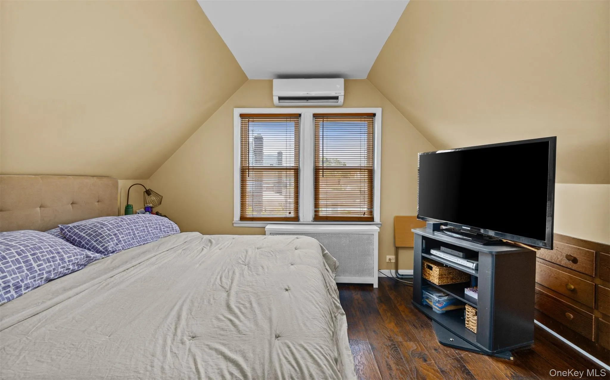 Bedroom featuring radiator heating unit, dark wood-type flooring, lofted ceiling, and an AC wall unit Bedroom featuring radiator heating unit, dark wood-type flooring, lofted ceiling, and an AC wall unit