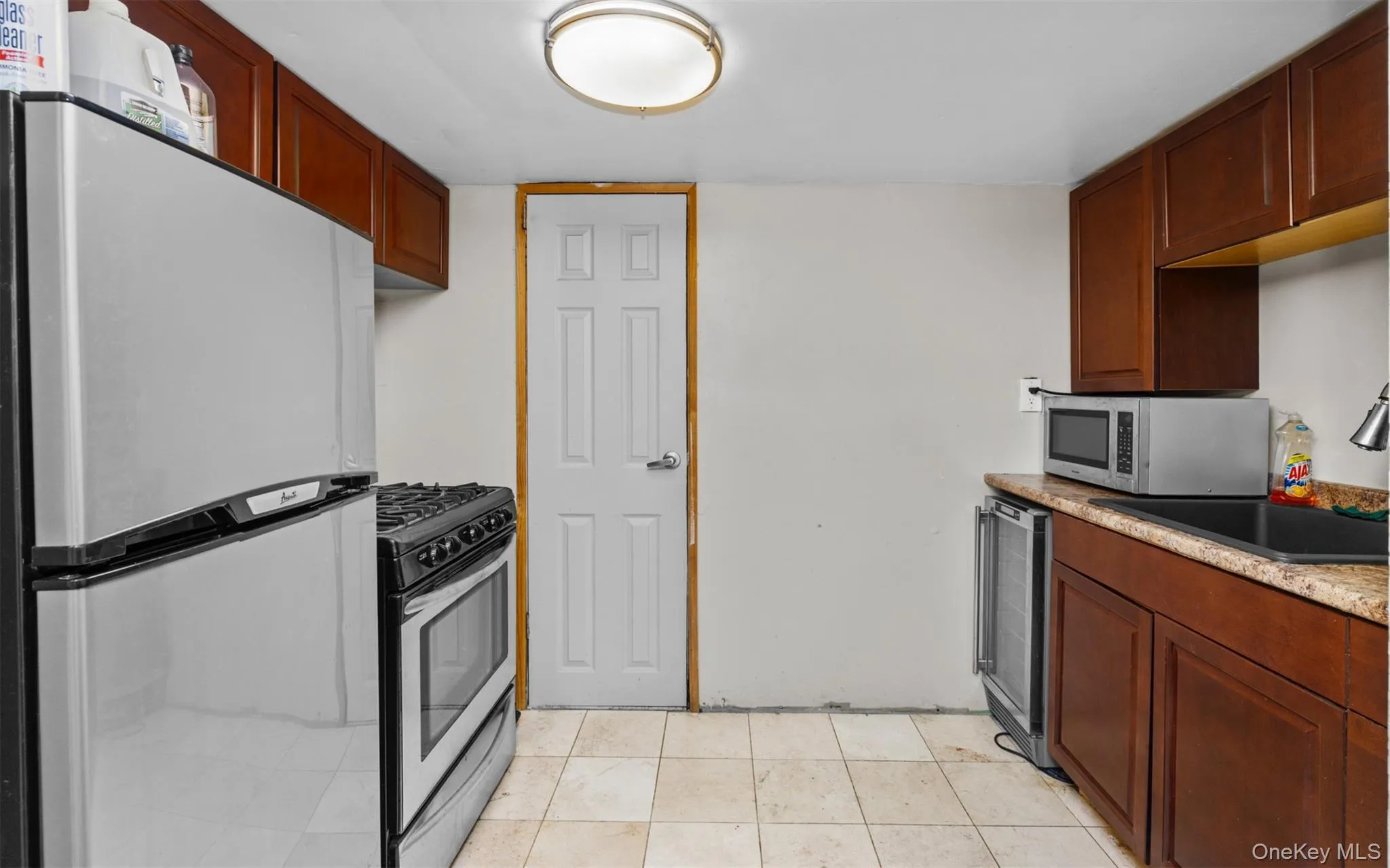 Kitchen featuring appliances with stainless steel finishes, light tile patterned floors, light stone countertops, and beverage cooler Kitchen featuring appliances with stainless steel finishes, light tile patterned floors, light stone countertops, and beverage cooler