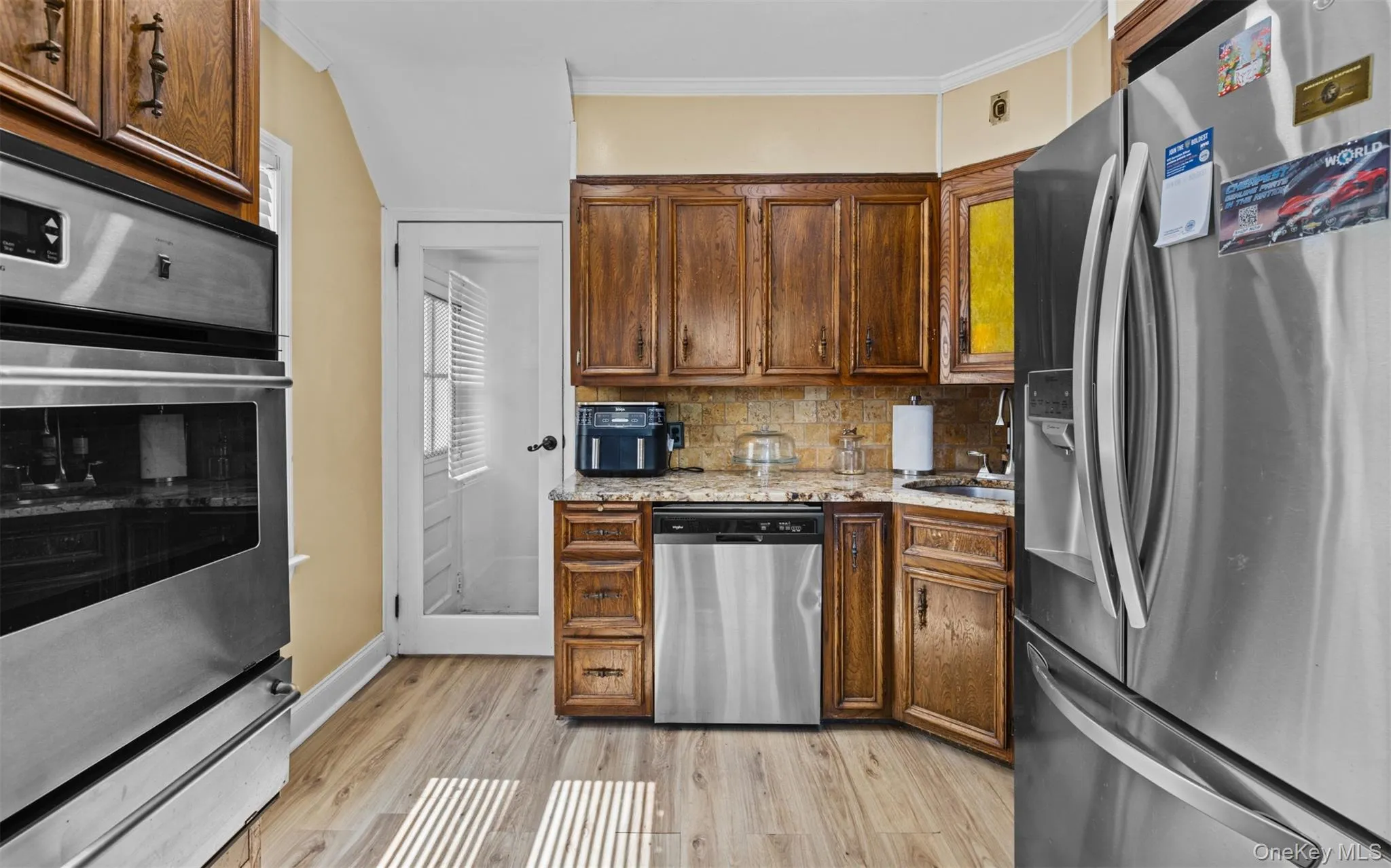 Kitchen featuring appliances with stainless steel finishes, decorative backsplash, light wood finished floors, ornamental molding, and a warming drawer Kitchen featuring appliances with stainless steel finishes, decorative backsplash, light wood finished floors, ornamental molding, and a warming drawer