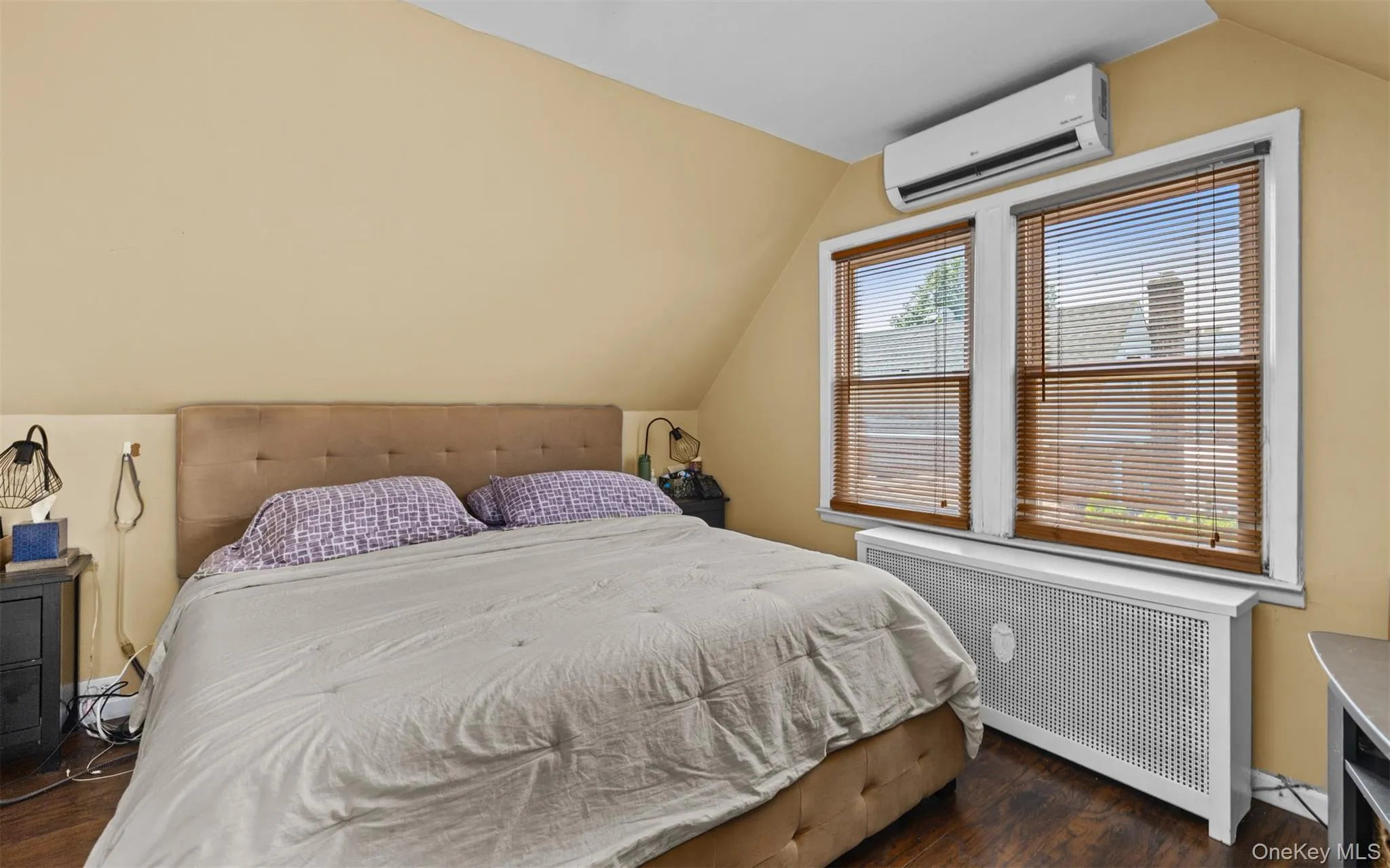 Bedroom with radiator, lofted ceiling, dark wood-style flooring, and a wall mounted air conditioner Bedroom with radiator, lofted ceiling, dark wood-style flooring, and a wall mounted air conditioner