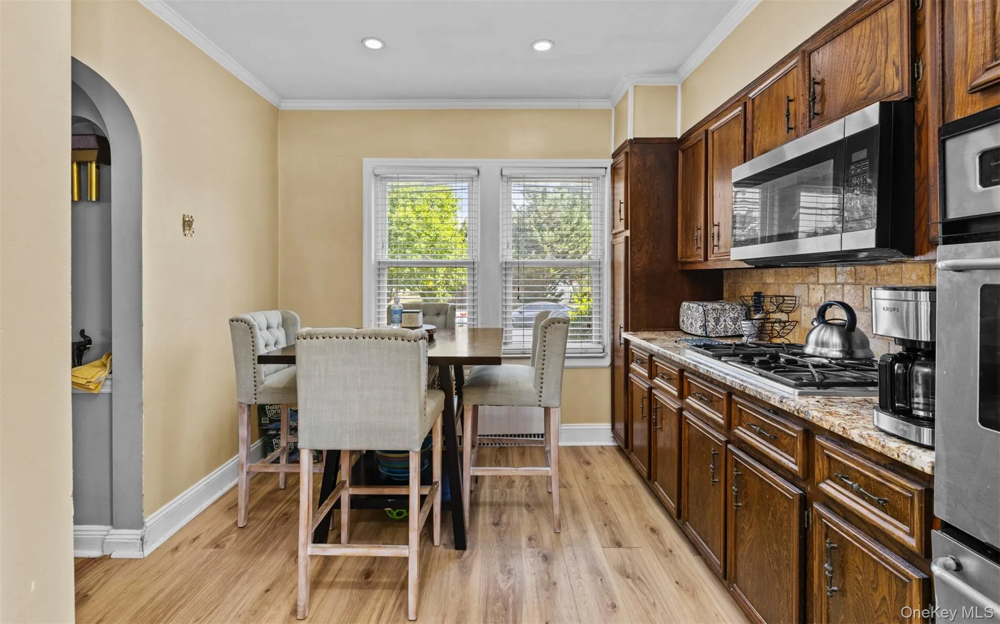 Kitchen featuring light wood-style floors, arched walkways, crown molding, light stone countertops, and stainless steel appliances Kitchen featuring light wood-style floors, arched walkways, crown molding, light stone countertops, and stainless steel appliances