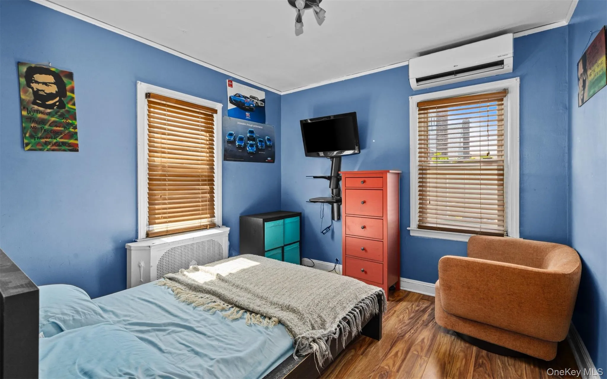 Bedroom featuring wood finished floors, a wall unit AC, radiator heating unit, and ornamental molding Bedroom featuring wood finished floors, a wall unit AC, radiator heating unit, and ornamental molding