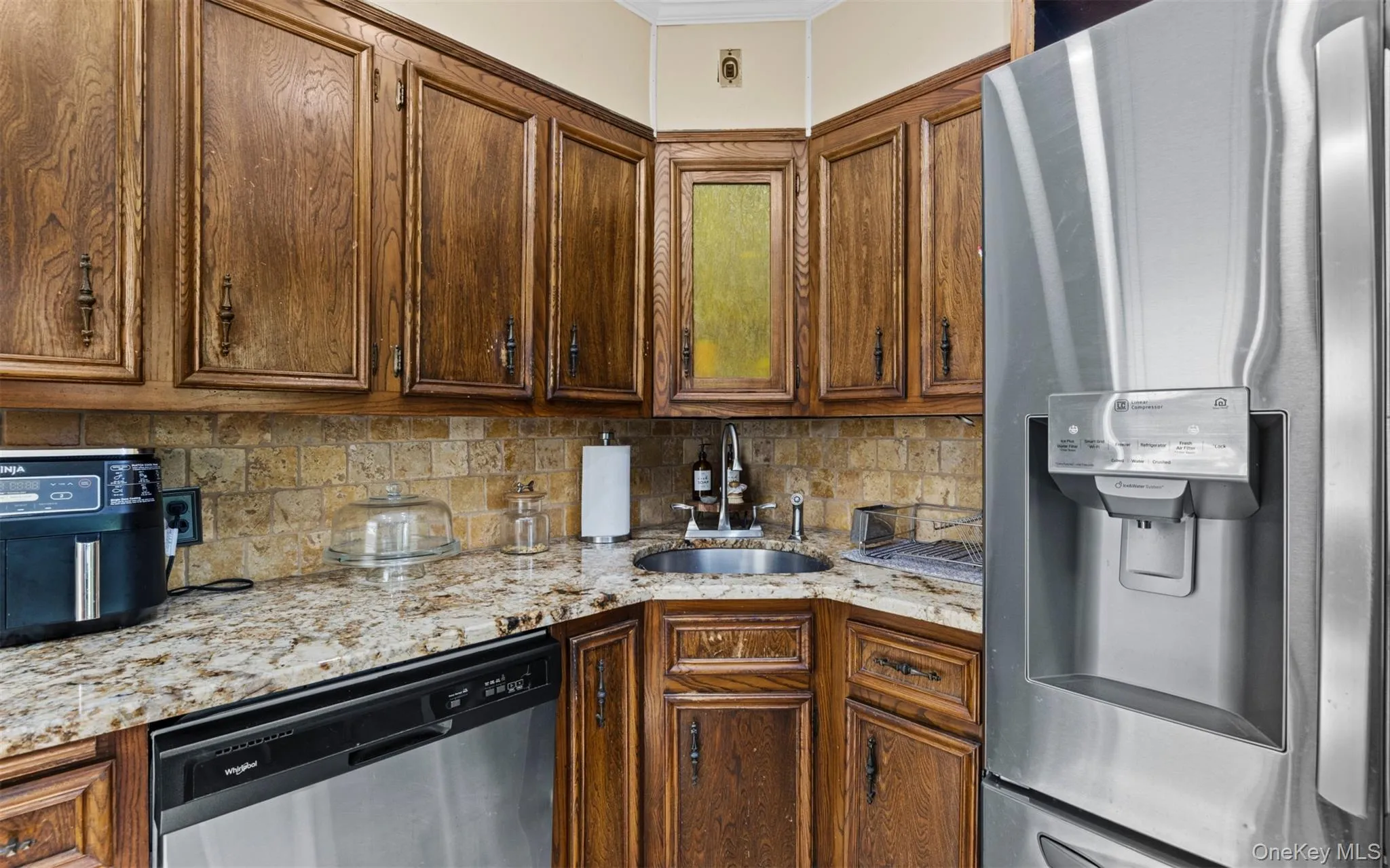 Kitchen featuring appliances with stainless steel finishes, light stone countertops, decorative backsplash, brown cabinets, and ornamental molding Kitchen featuring appliances with stainless steel finishes, light stone countertops, decorative backsplash, brown cabinets, and ornamental molding