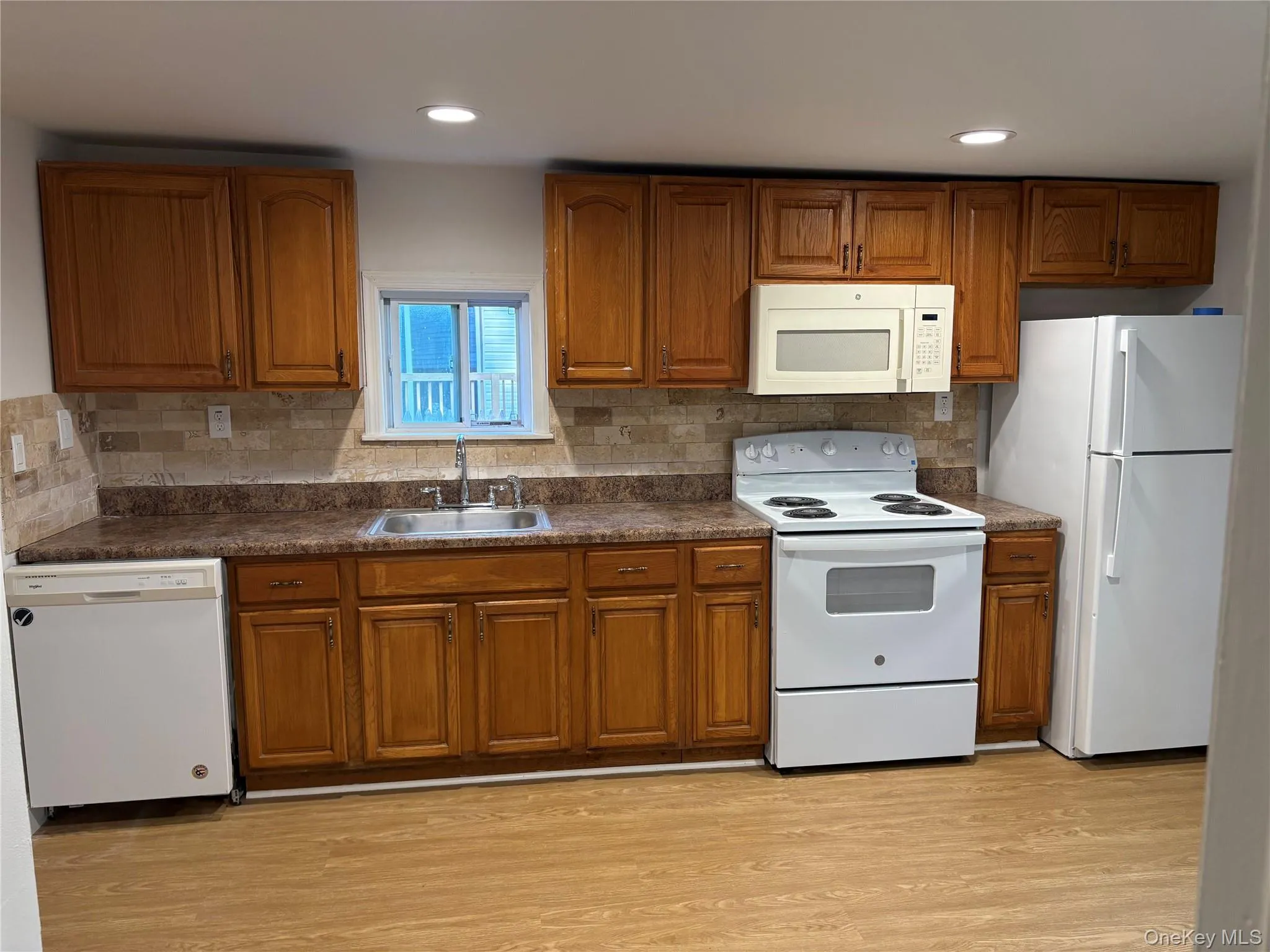 Kitchen featuring white appliances, brown cabinets, dark countertops, and recessed lighting Kitchen featuring white appliances, brown cabinets, dark countertops, and recessed lighting