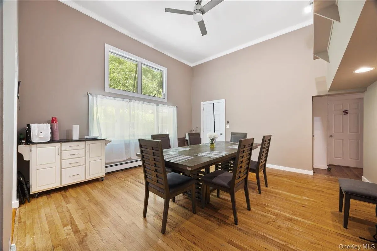 Dining room featuring light wood finished floors, ornamental molding, a baseboard radiator, a ceiling fan, and a towering ceiling Dining room featuring light wood finished floors, ornamental molding, a baseboard radiator, a ceiling fan, and a towering ceiling
