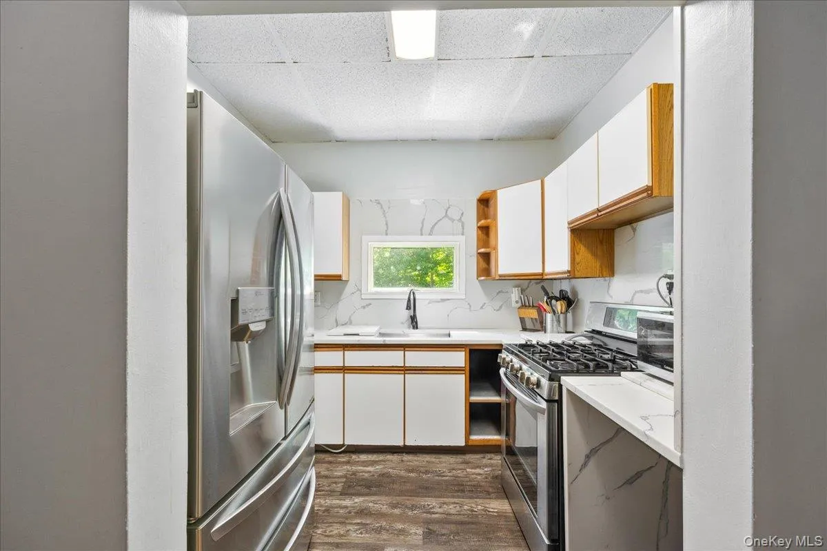 Kitchen featuring brown cabinetry, light countertops, white cabinets, open shelves, and a drop ceiling Kitchen featuring brown cabinetry, light countertops, white cabinets, open shelves, and a drop ceiling