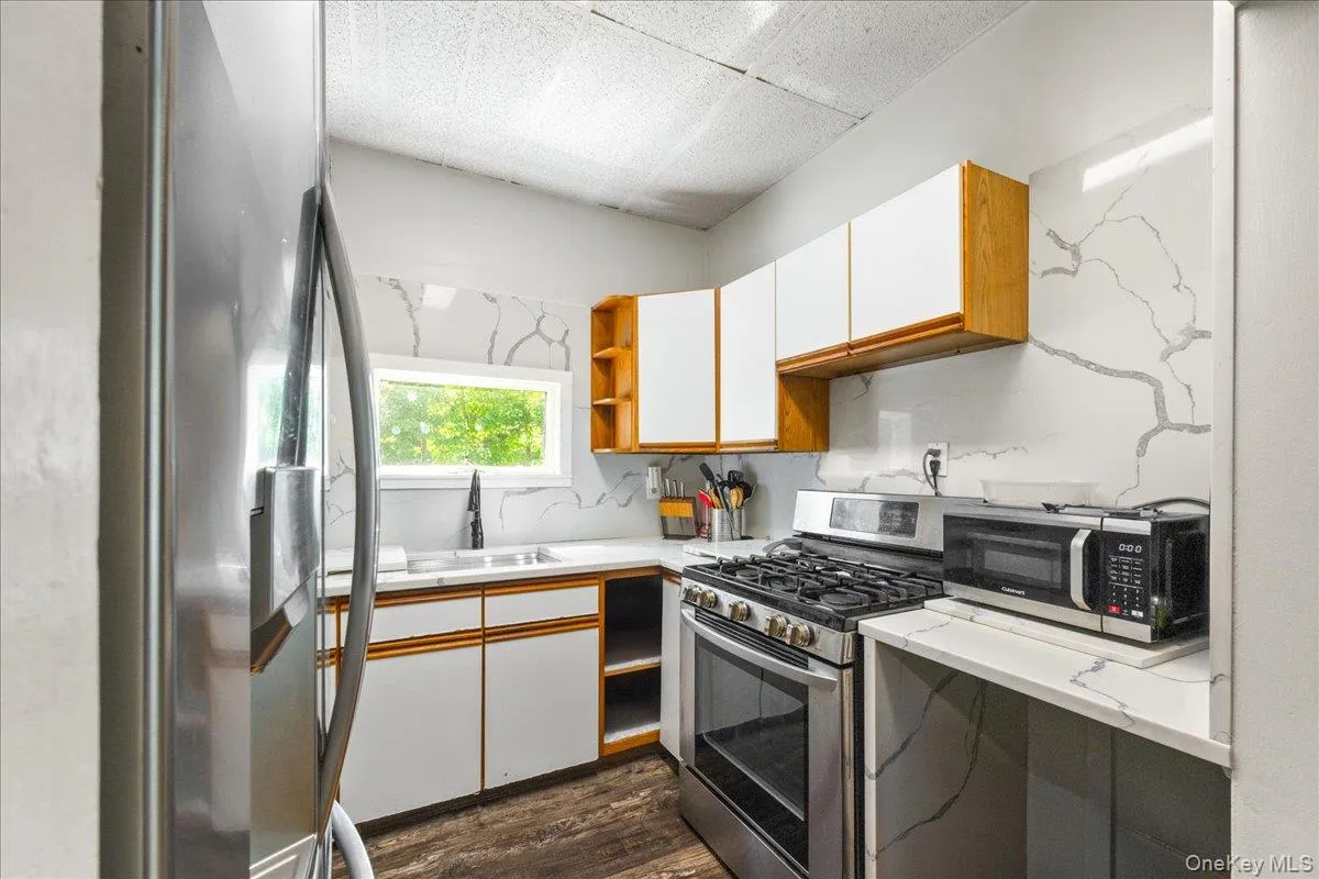 Kitchen featuring brown cabinets, white cabinets, light countertops, appliances with stainless steel finishes, and open shelves Kitchen featuring brown cabinets, white cabinets, light countertops, appliances with stainless steel finishes, and open shelves
