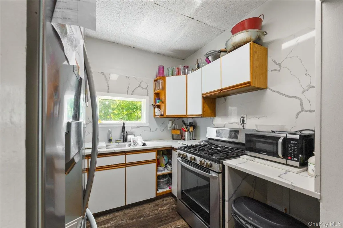 Kitchen featuring brown cabinetry, white cabinetry, light countertops, stainless steel appliances, and dark wood-style floors Kitchen featuring brown cabinetry, white cabinetry, light countertops, stainless steel appliances, and dark wood-style floors