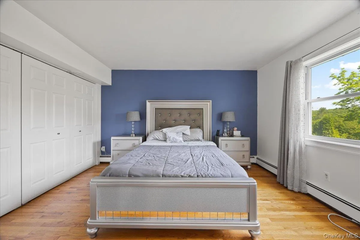 Bedroom with wood finished floors, baseboard heating, and a closet Bedroom with wood finished floors, baseboard heating, and a closet