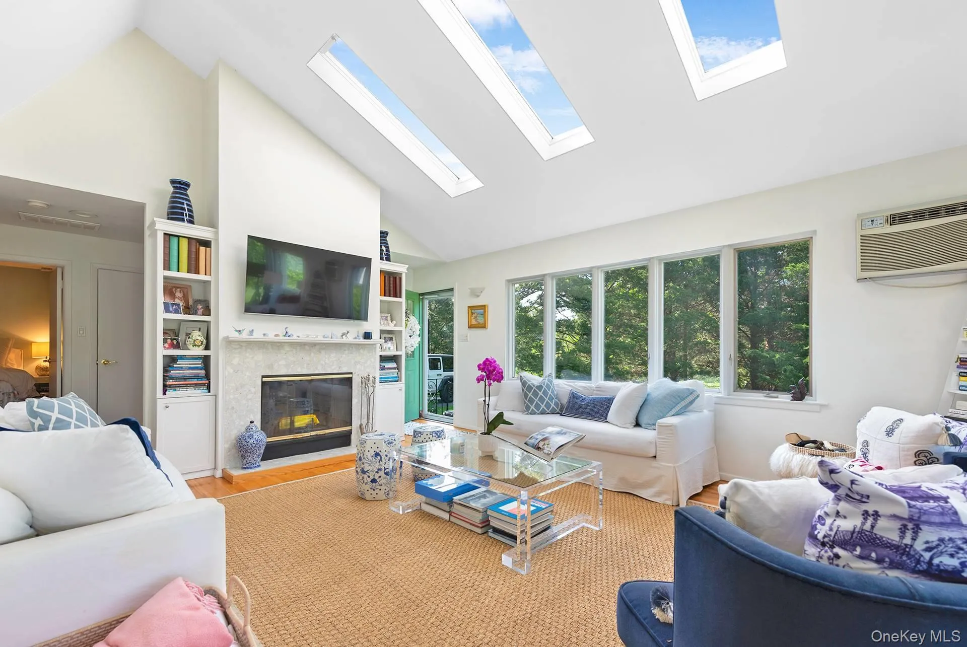 Living area with high vaulted ceiling, wood finished floors, a skylight, a fireplace, and an AC wall unit Living area with high vaulted ceiling, wood finished floors, a skylight, a fireplace, and an AC wall unit