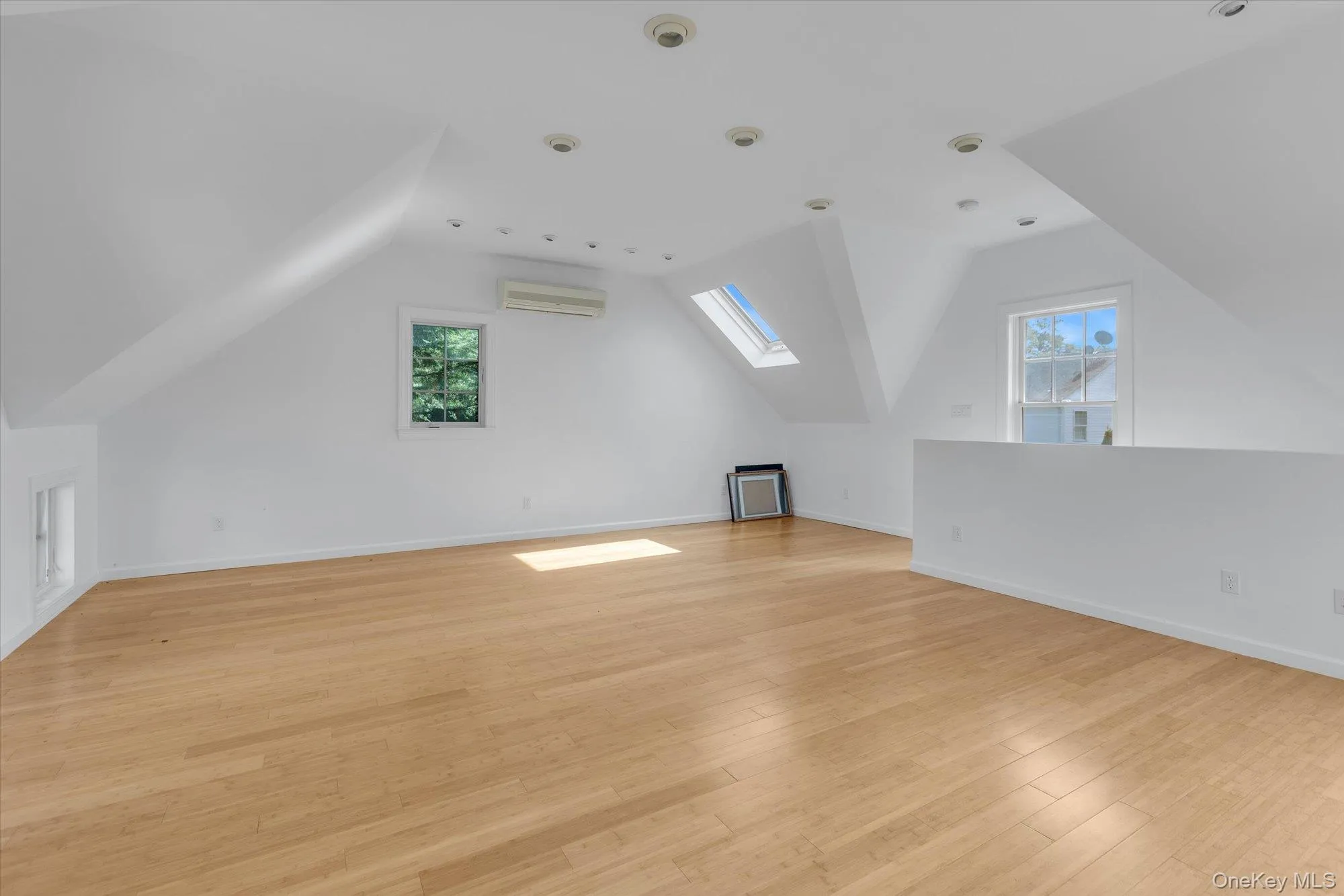 Additional living space featuring vaulted ceiling, a skylight, light wood finished floors, and a wall mounted air conditioner Additional living space featuring vaulted ceiling, a skylight, light wood finished floors, and a wall mounted air conditioner