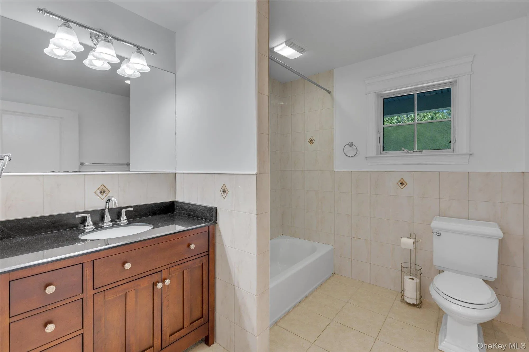 Bathroom featuring vanity, tile walls, shower / washtub combination, and light tile patterned flooring Bathroom featuring vanity, tile walls, shower / washtub combination, and light tile patterned flooring