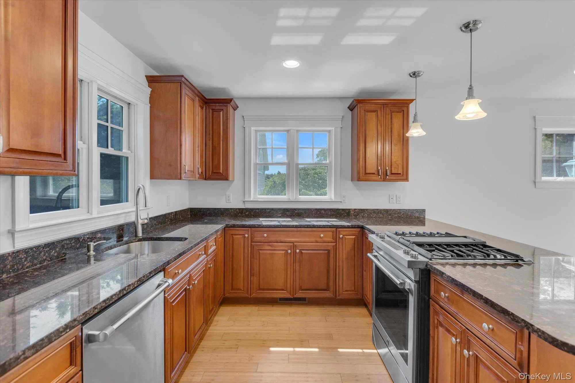 Kitchen with brown cabinetry, appliances with stainless steel finishes, dark stone countertops, and recessed lighting Kitchen with brown cabinetry, appliances with stainless steel finishes, dark stone countertops, and recessed lighting