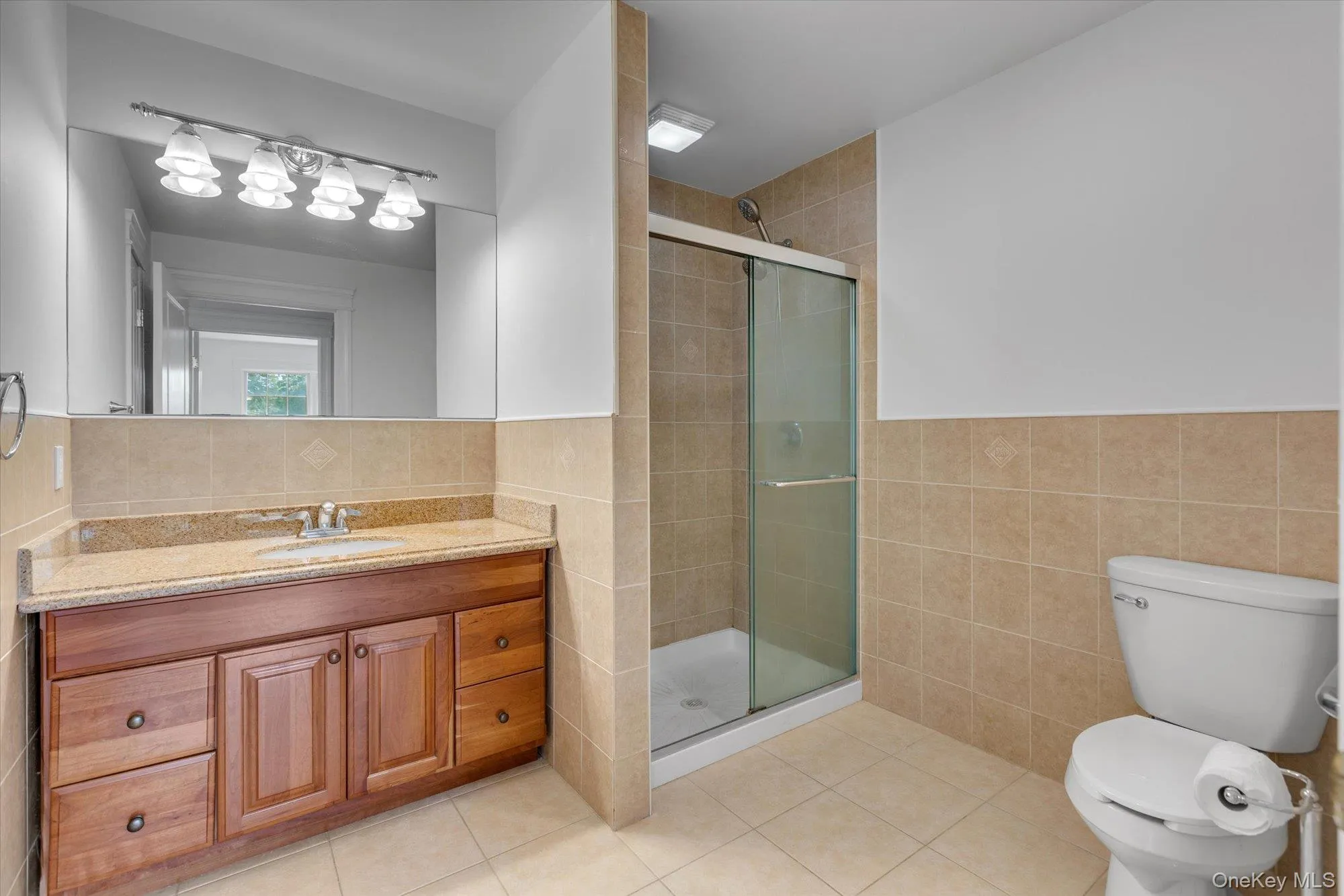 Bathroom with tile walls, vanity, a wainscoted wall, a shower stall, and light tile patterned floors Bathroom with tile walls, vanity, a wainscoted wall, a shower stall, and light tile patterned floors